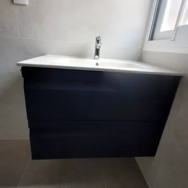 Tocador de baño azul oscuro con encimera blanca y grifo plateado contra una pared gris claro.