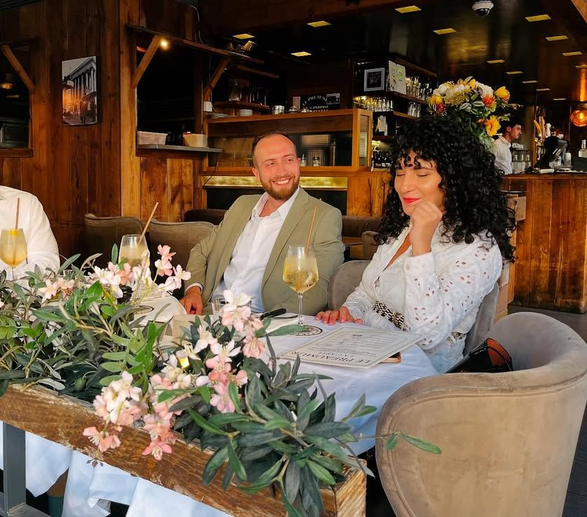Un homme en blazer et une femme aux cheveux bouclés sont assis à une table