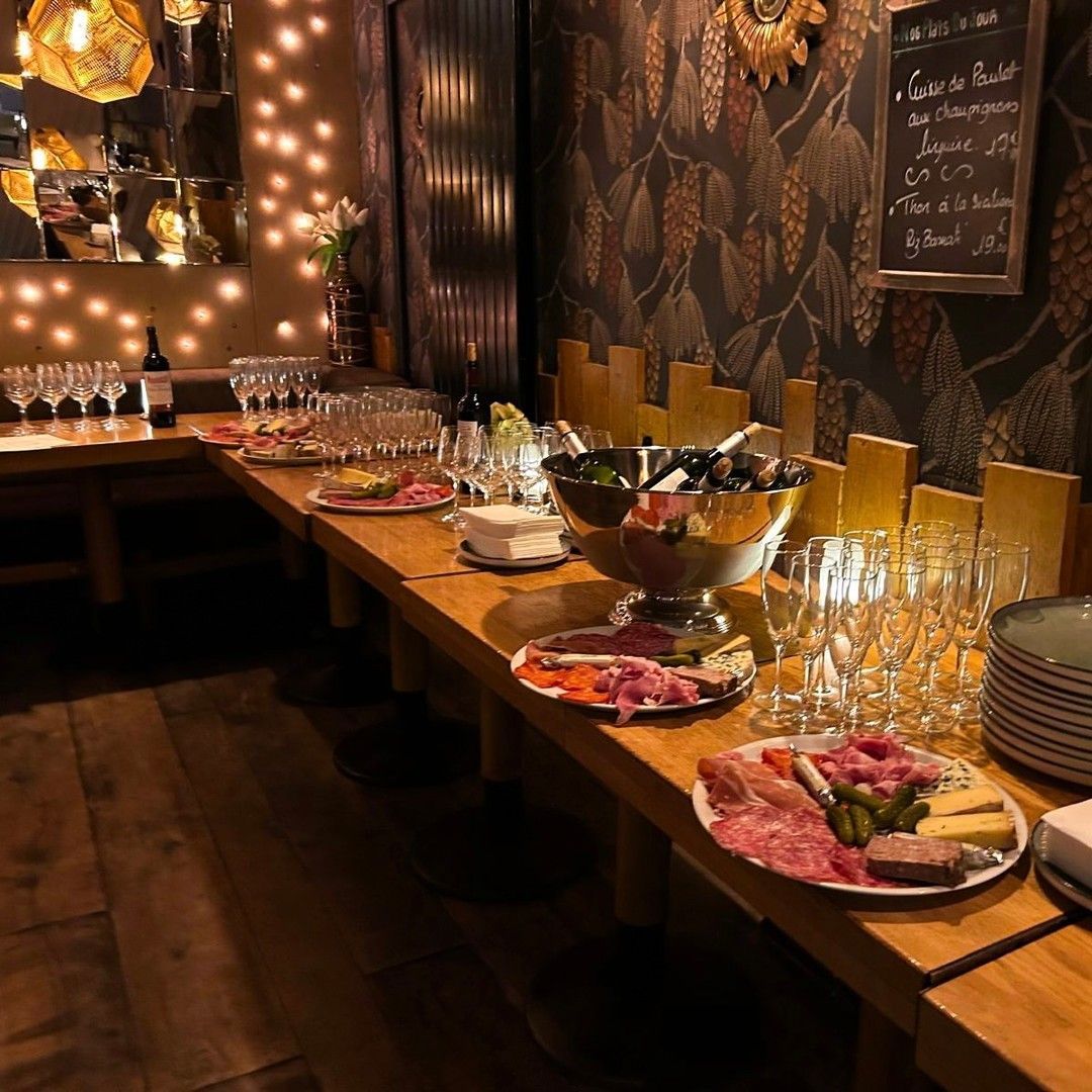 Un bar-restaurant chaleureux et tamisé propose une table en bois dressée avec des assiettes de charcuterie et des verres.