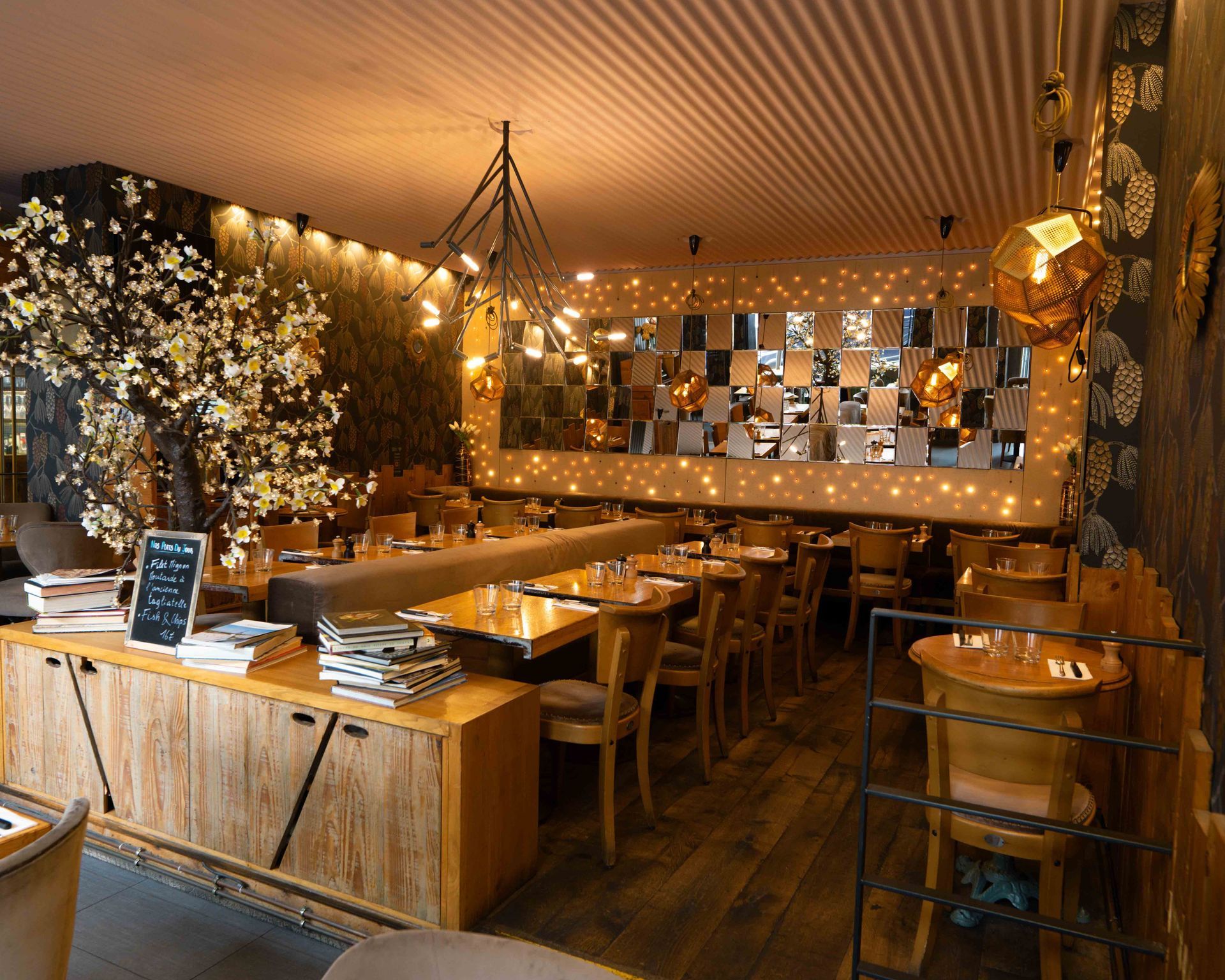 Intérieur de restaurant à l'éclairage chaleureux, avec mobilier en bois, cerisier décoratif en fleurs et mur recouvert de miroirs.