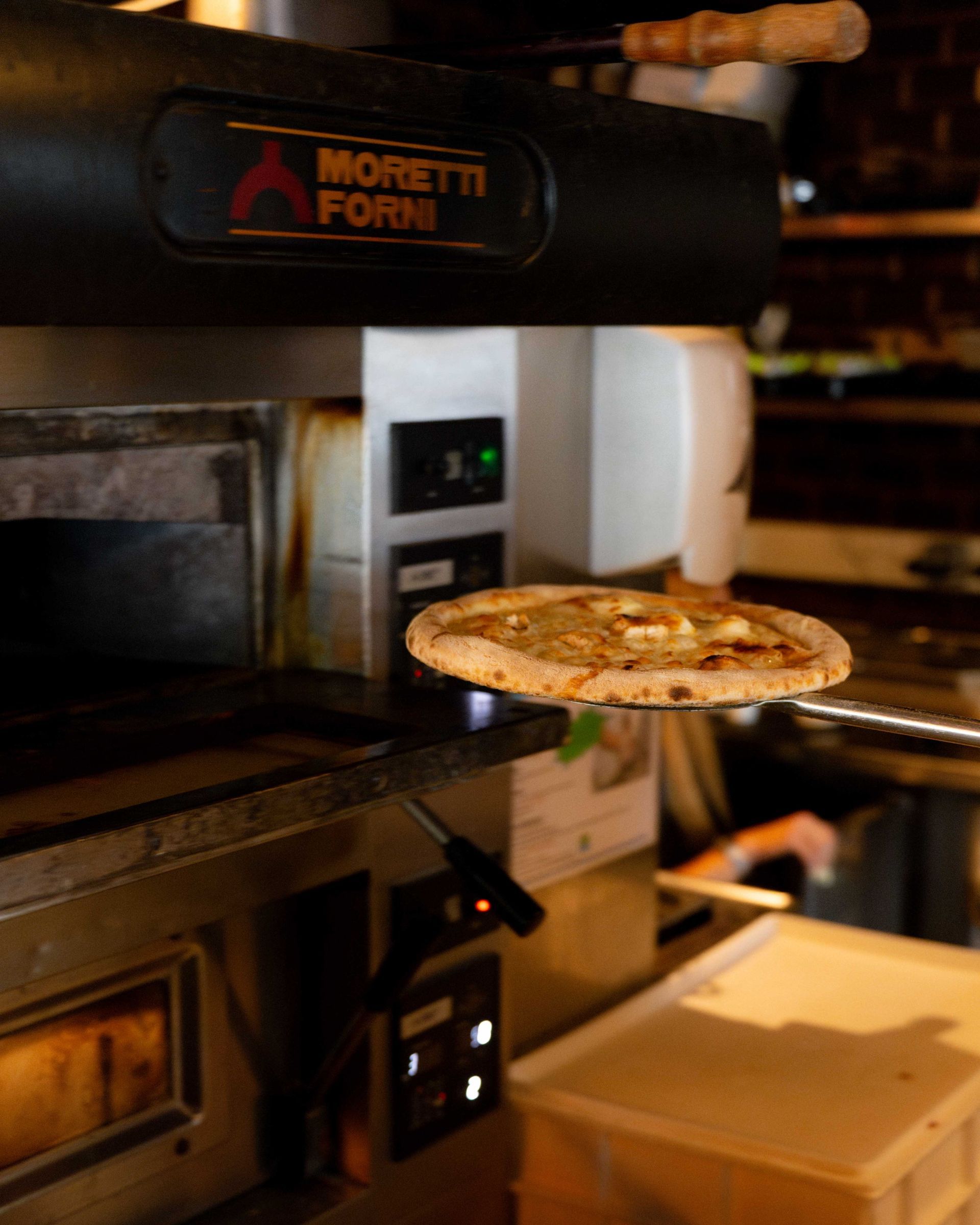 Une pizza est sortie d'un four commercial Moretti Forni à l'aide d'une pelle métallique.