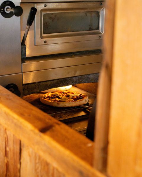 Une pizza en train de cuire dans un four industriel, vue à travers une ouverture lambrissée.