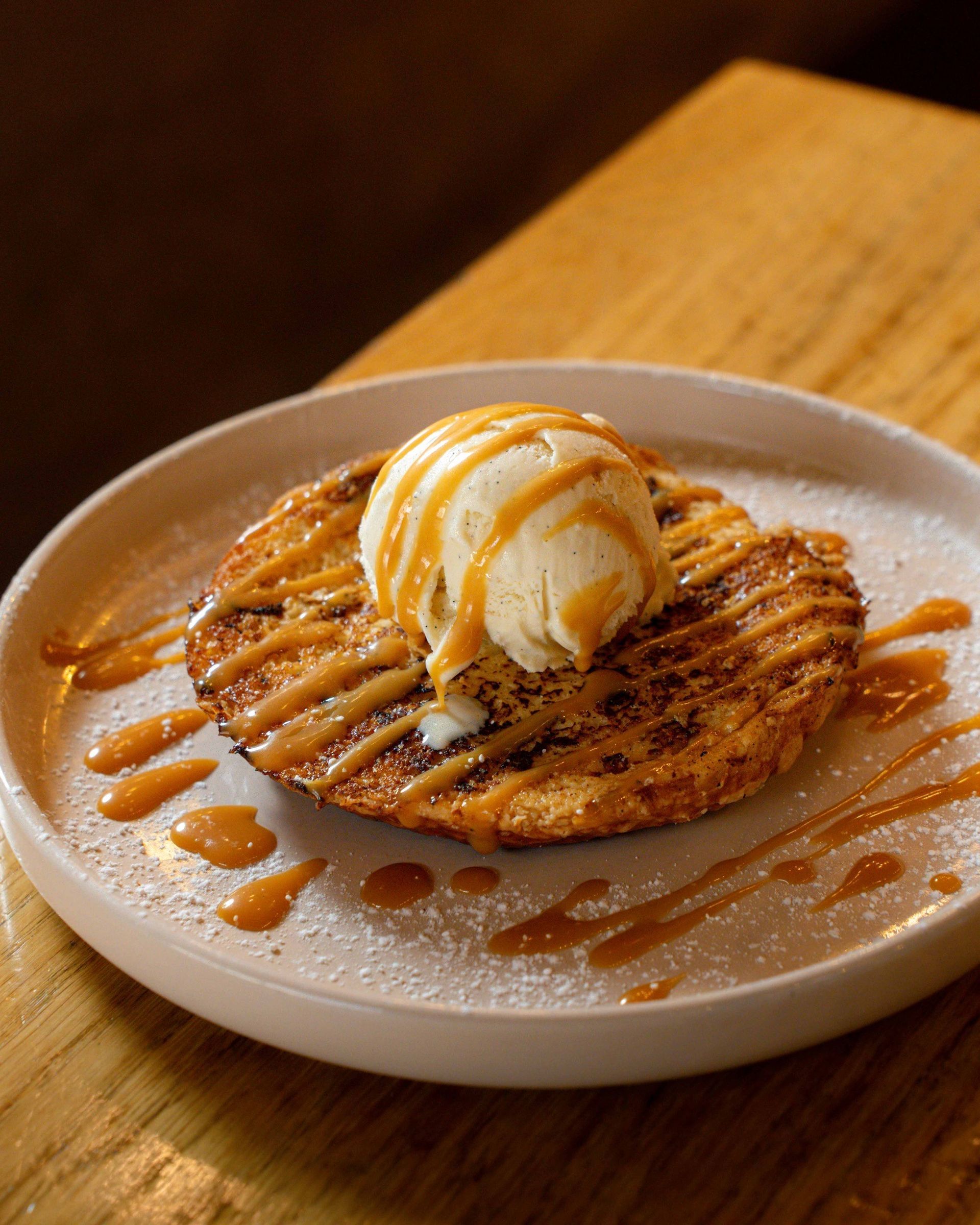 Un biscuit chaud garni d'une boule de glace à la vanille et nappé de sauce au caramel, servi dans une assiette.