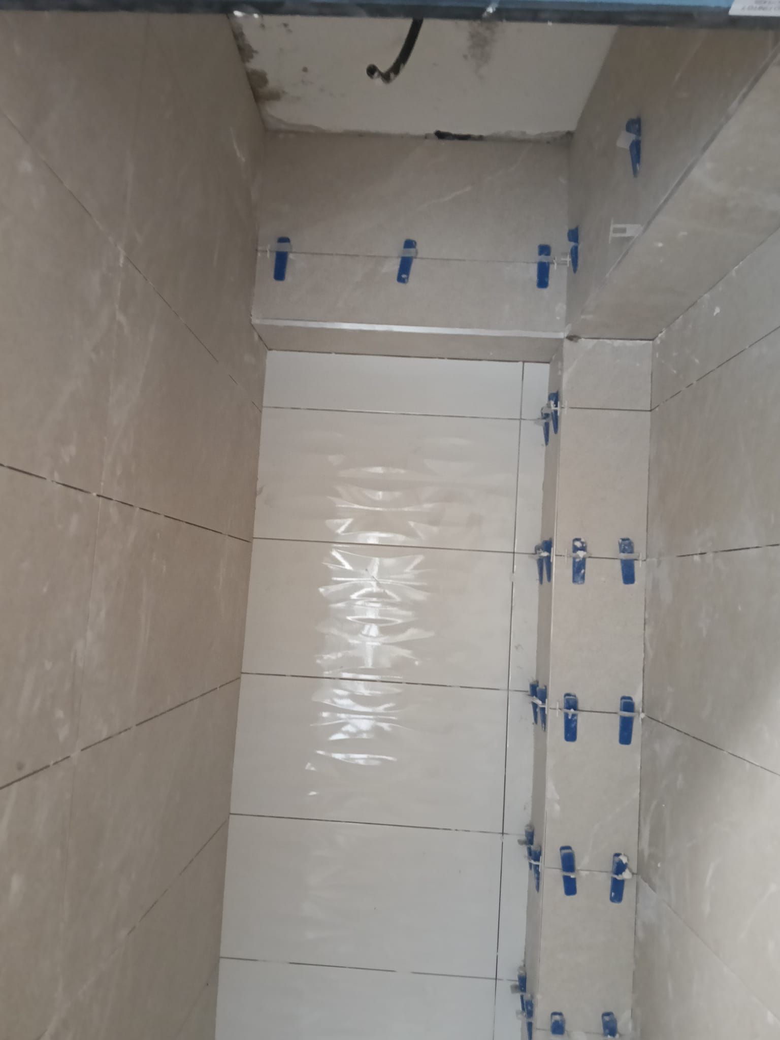 Rincón de baño alicatado con una puerta blanca y cinta protectora azul en las paredes y los accesorios