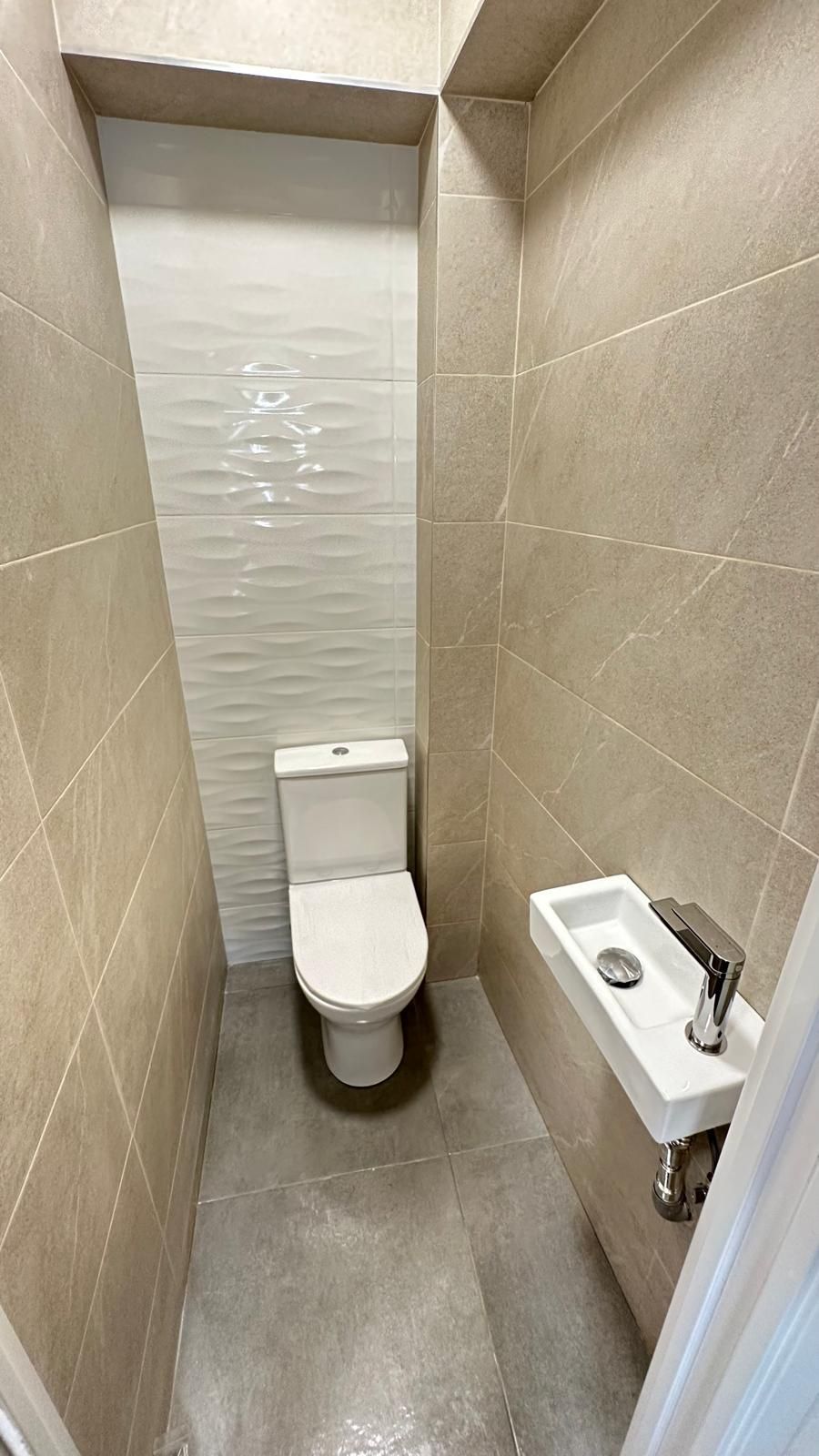 Aseo estrecho alicatado, con un inodoro y un pequeño lavabo de pared.