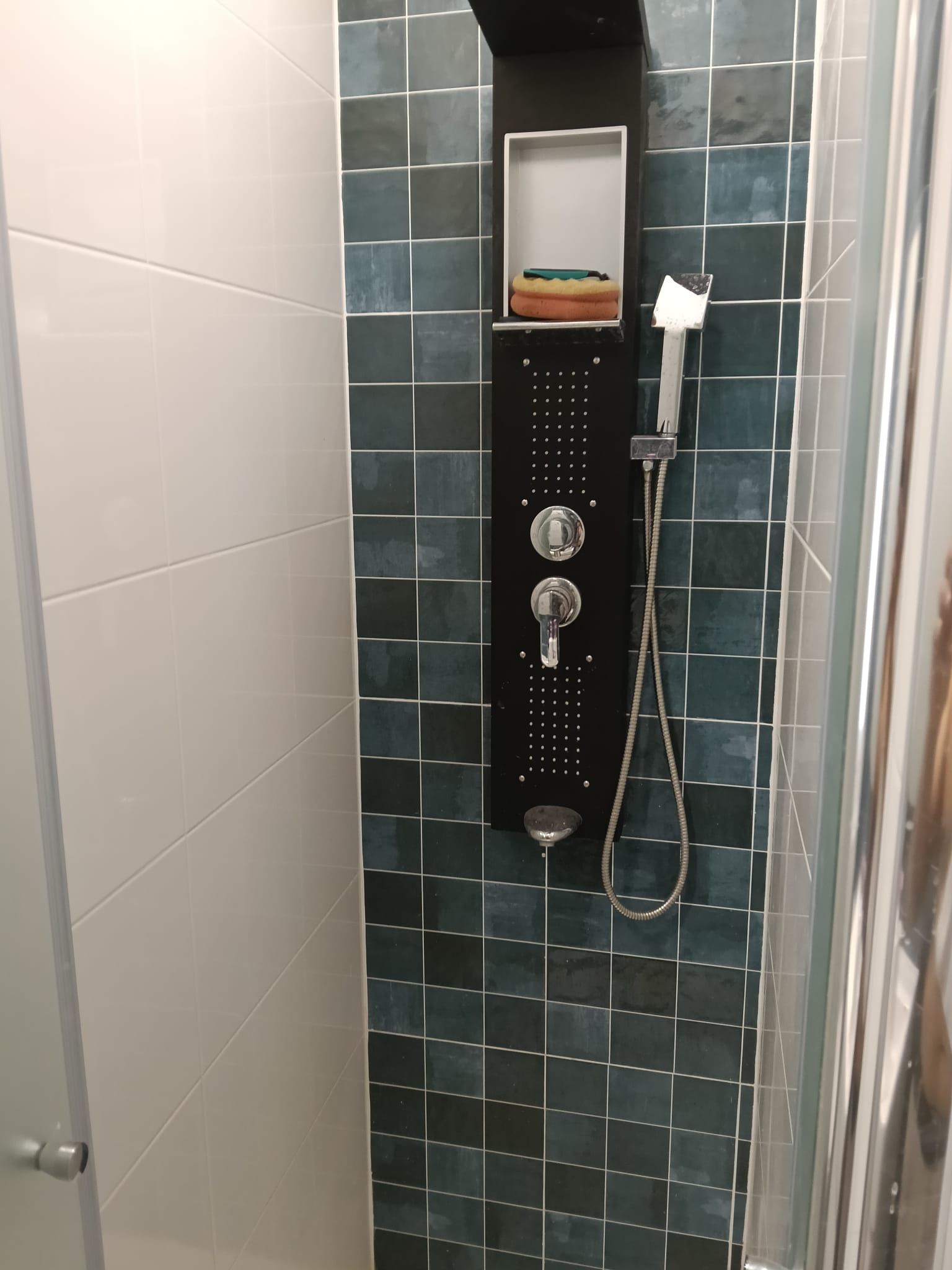 Ducha de baño con mandos negros de pared, ducha de mano y una pared de acento con azulejos verde azulado.