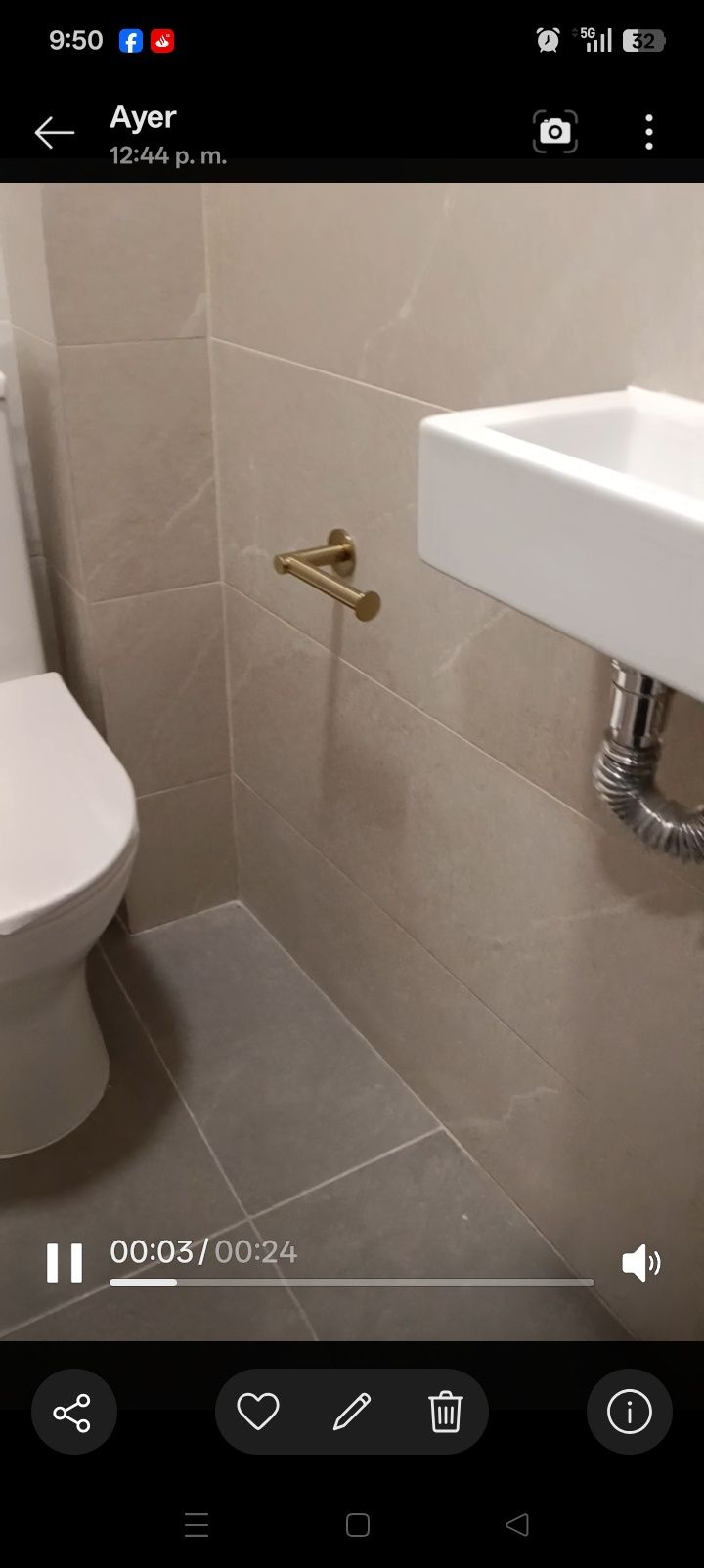 Cuarto de baño pequeño con un lavabo de pared, el borde del inodoro y una barra de apoyo de latón junto a las paredes revestidas de azulejos beige.