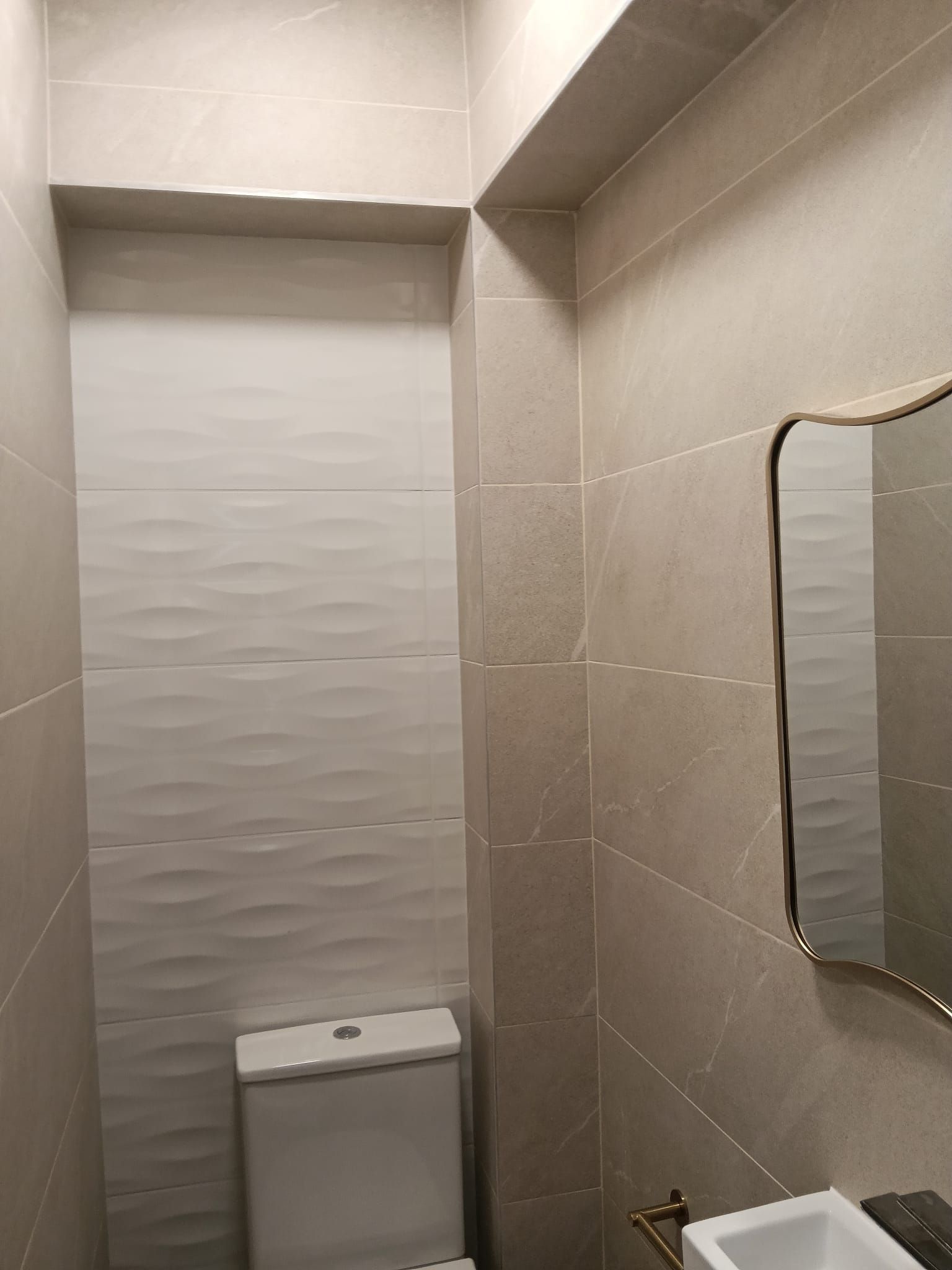 Cuarto de baño pequeño con azulejos beige, un inodoro debajo de una ventana y un espejo parcial a la derecha.