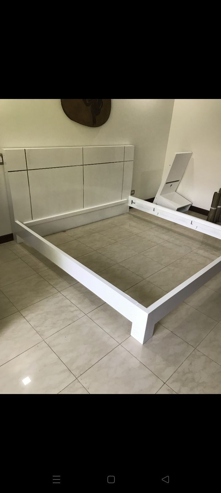 Estructura de cama blanca con colchón gris en una esquina de un dormitorio con suelo de baldosas
