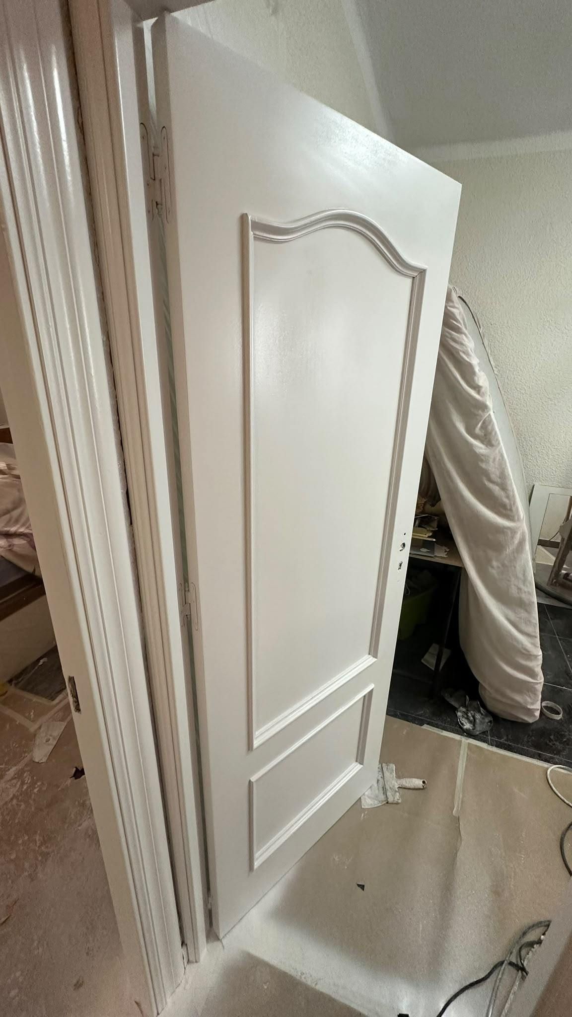 Puerta blanca con paneles entreabierta en una habitación desordenada, con una manguera de aspiradora y herramientas cerca.