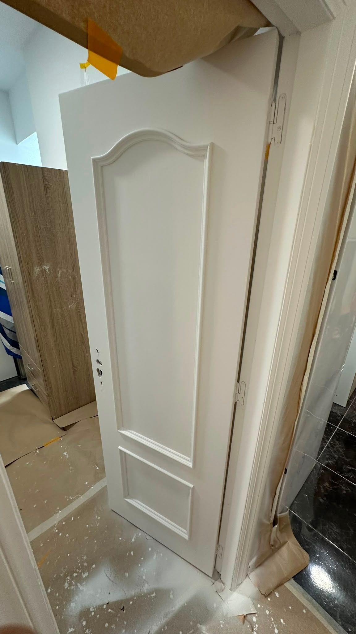 Puerta blanca de armario de interior con paneles y molduras decorativas, apoyada en un vano durante una renovación del hogar