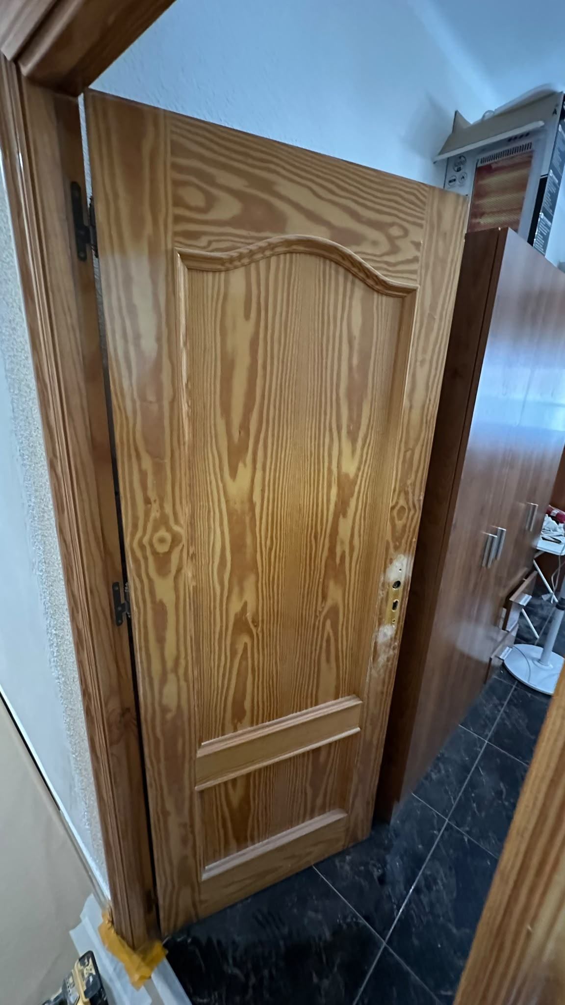 Puerta de baño de madera con paneles, entreabierta en un pasillo estrecho con azulejos