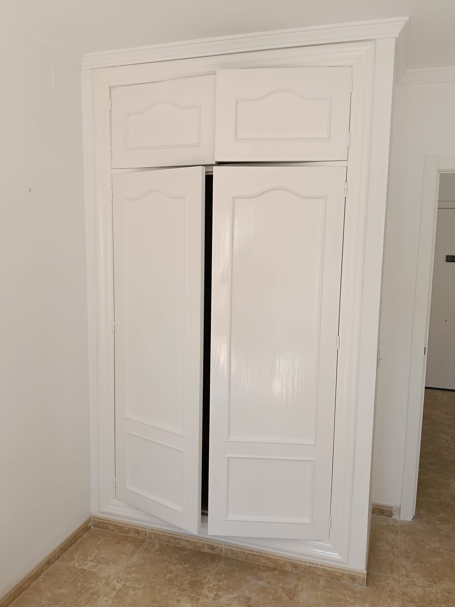 Armario empotrado blanco con puertas correderas parcialmente abiertas en una habitación beige.