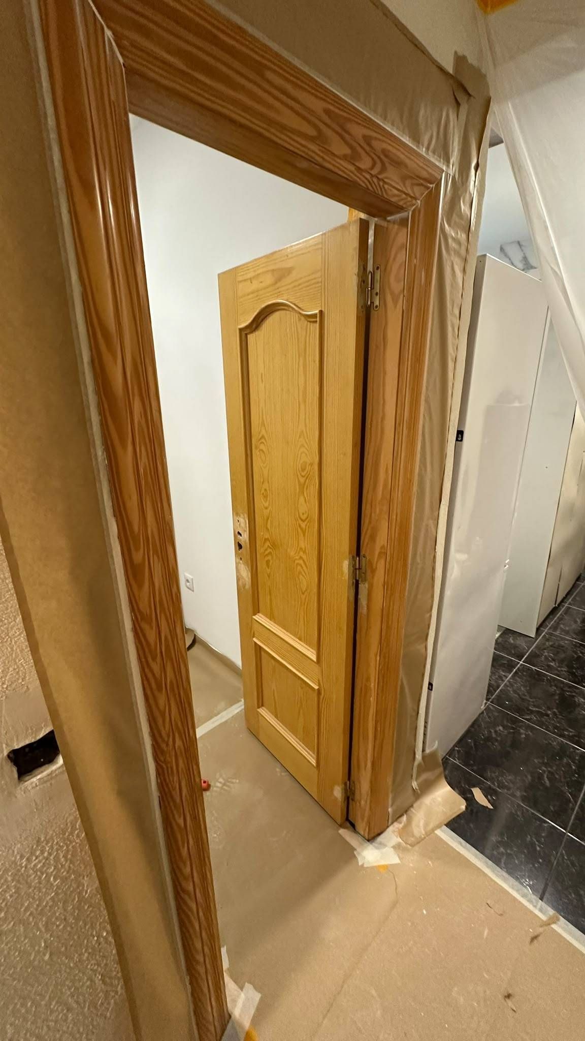 Pasillo estrecho con una puerta de madera abierta junto a una escalera.
