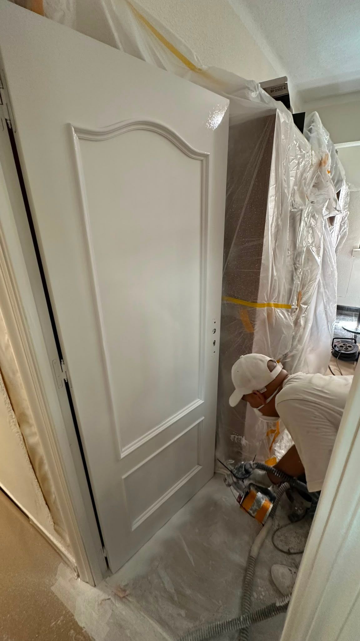 Una persona pintando una puerta blanca en el pasillo de una casa, con herramientas y lonas protectoras cerca