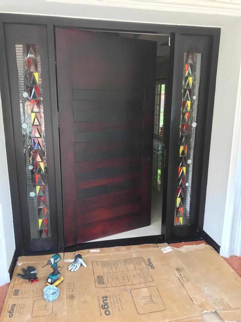 Puerta de entrada oscura con paneles laterales de vidrieras y una plancha de cartón en el suelo, en el interior