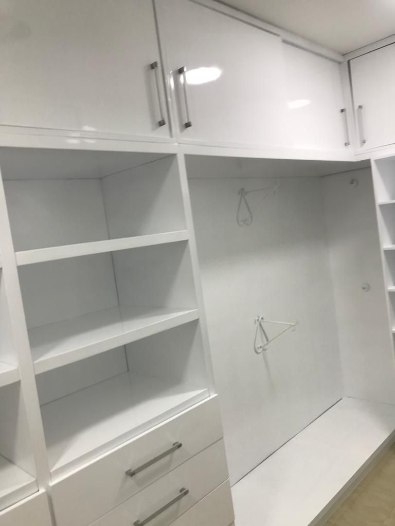 Armario empotrado blanco con estantes, cajones y barras para colgar en una habitación luminosa.