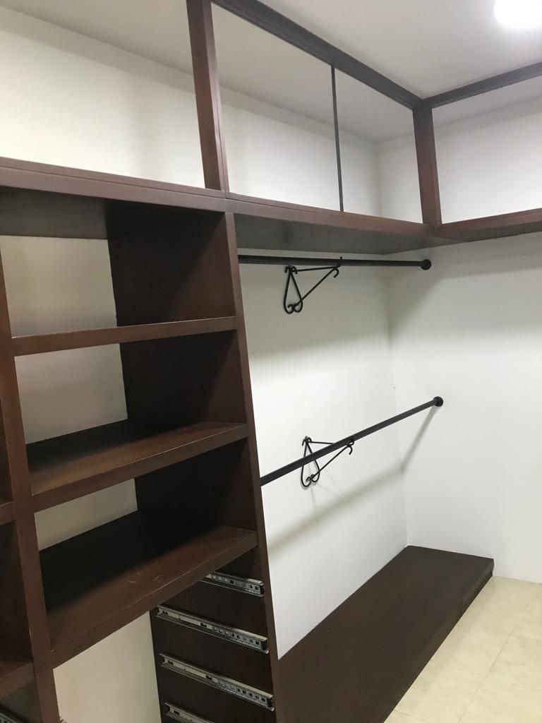 Vestidor vacío con estantes marrones, barras para colgar ropa y un banco empotrado sobre un suelo beige.