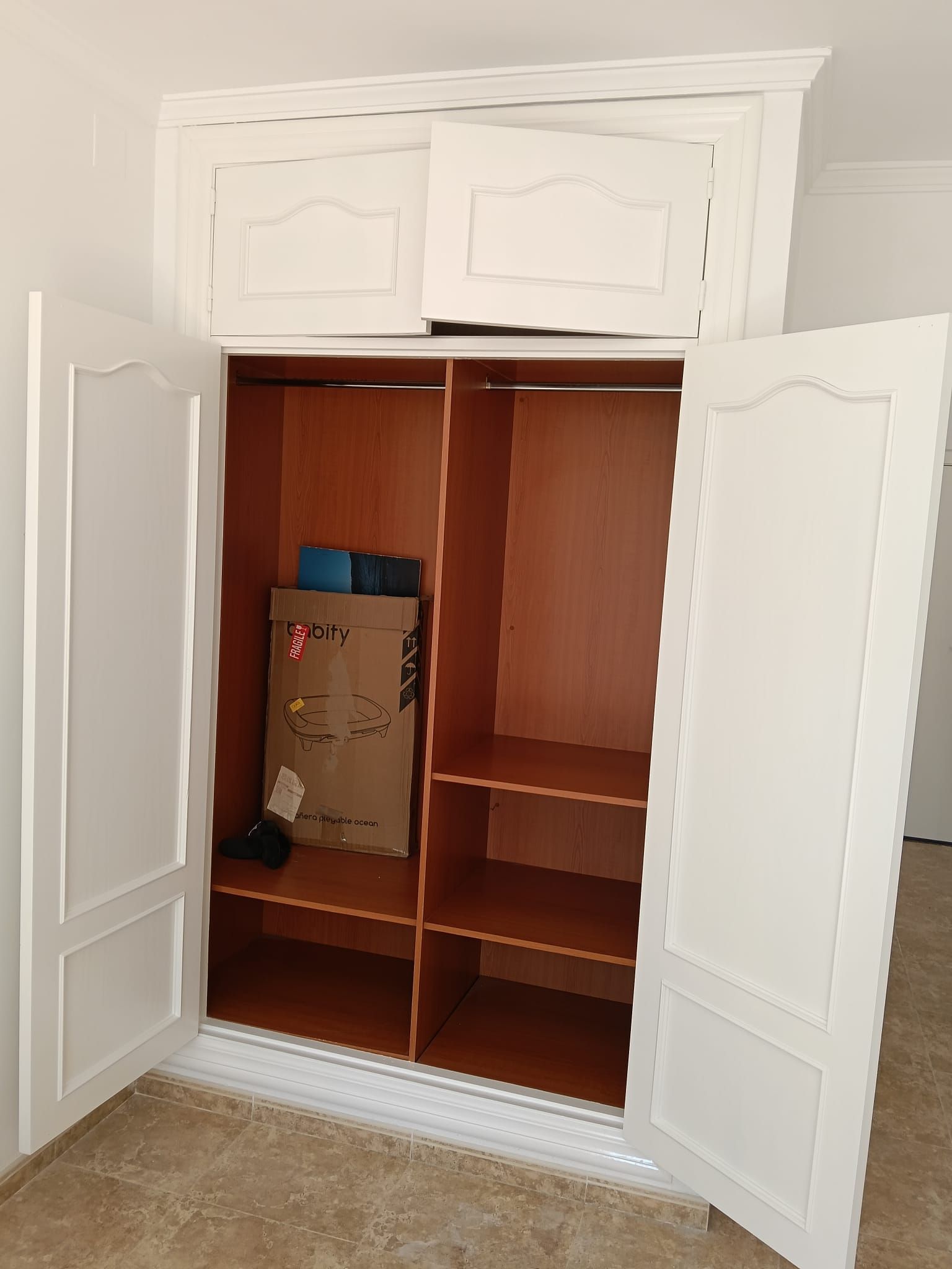 Armario blanco abierto con estantes de madera empotrados, una bolsa en su interior y suelo enmoquetado de color beige.