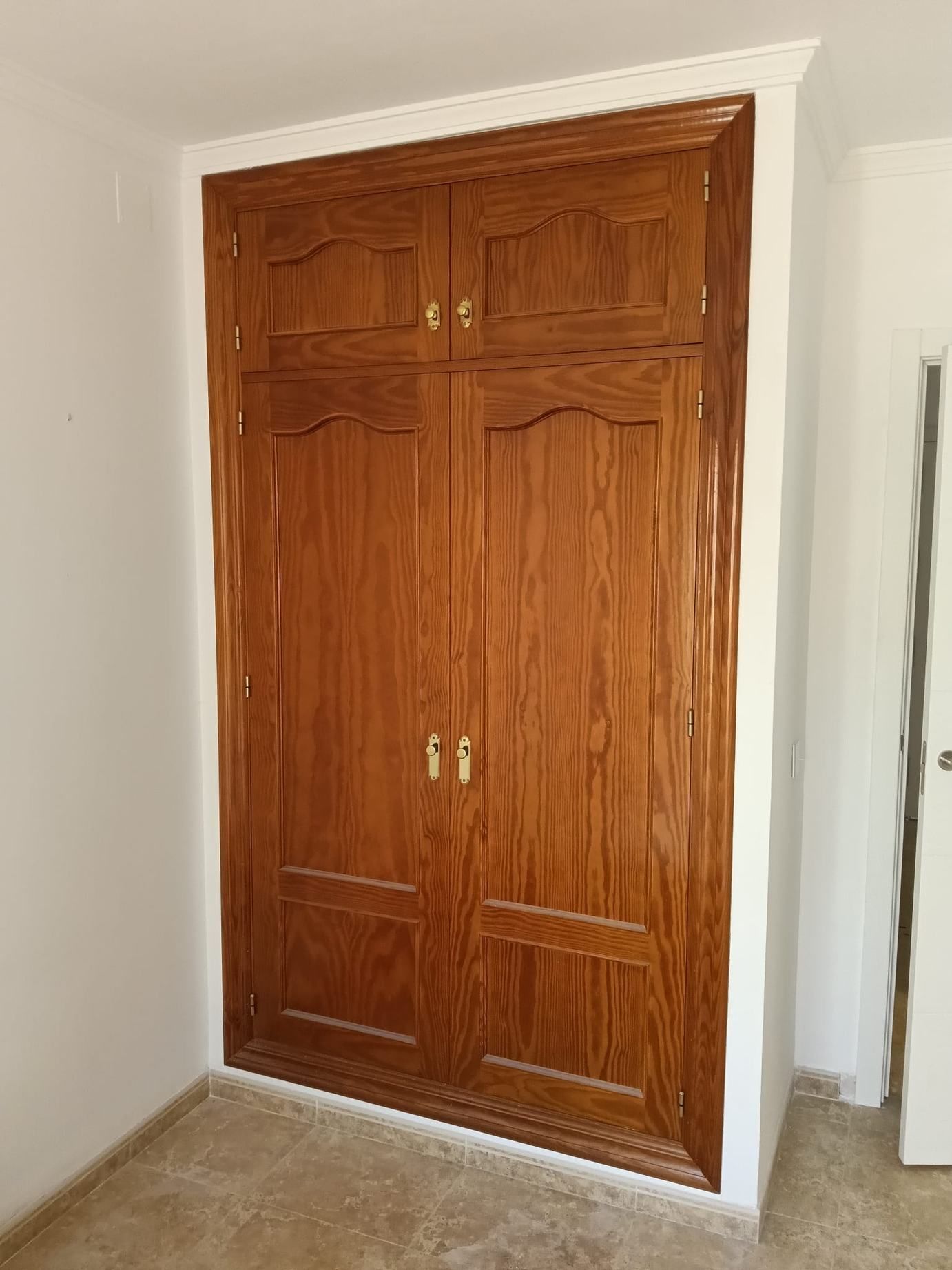 Puertas de armario de madera con paneles decorativos en una habitación blanca.