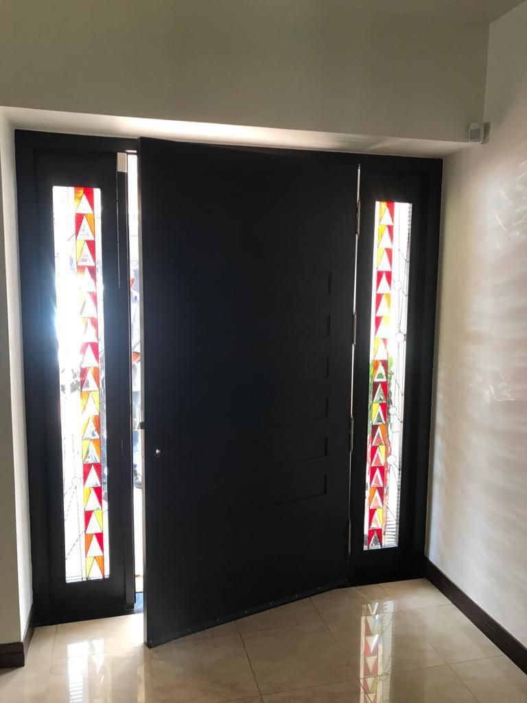 Puerta principal abierta con estrechas ventanas laterales de vidrieras en un pasillo.