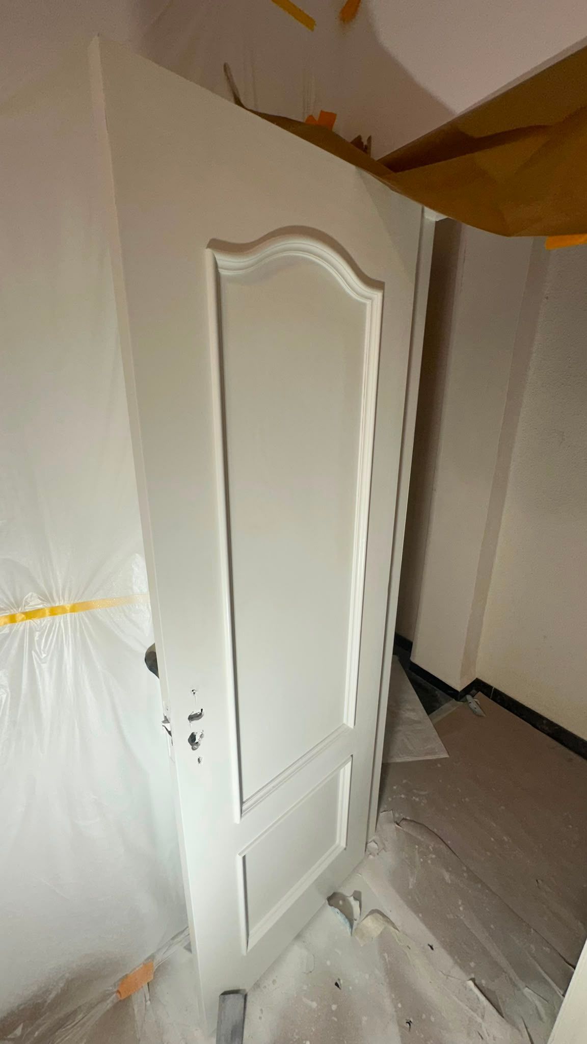 Puerta blanca de interior apoyada en una habitación parcialmente cubierta durante una reforma