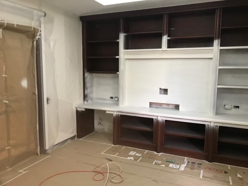 Mueble multimedia empotrado con estantes de madera oscura y panel central blanco en una habitación sin terminar