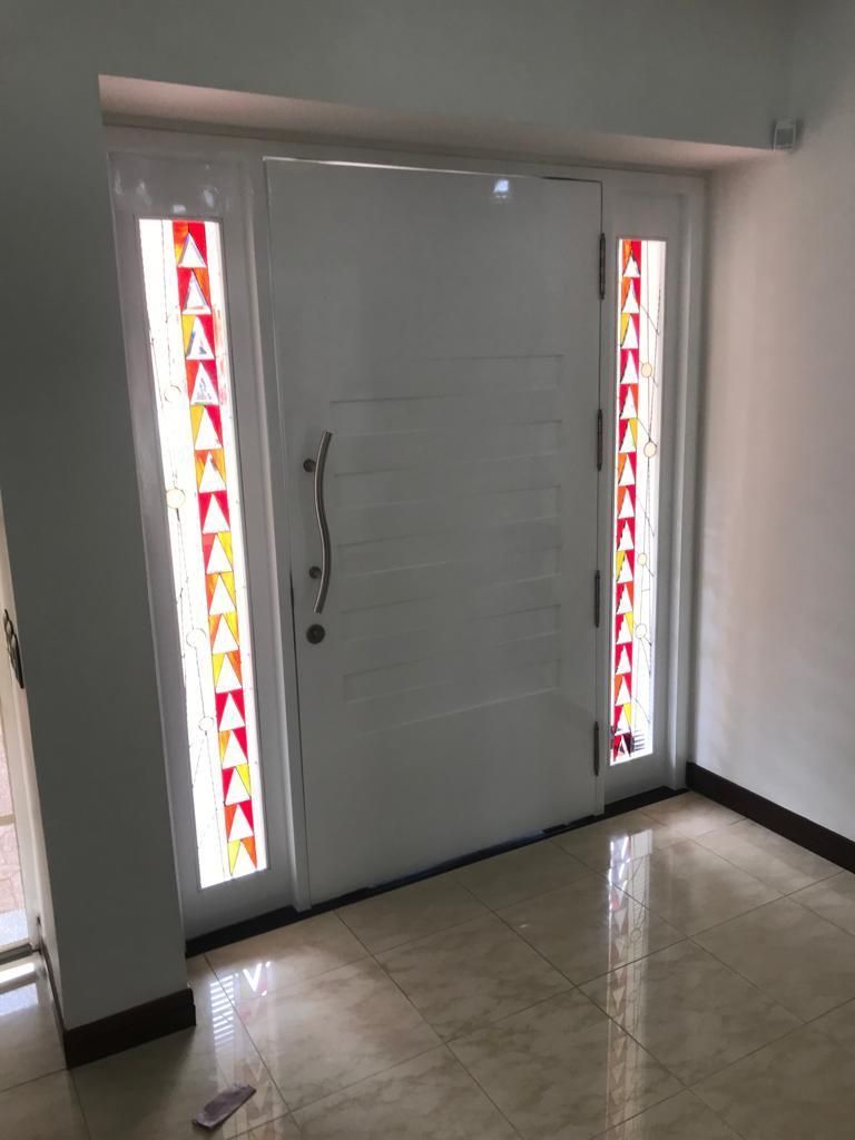 Entrada principal con puertas dobles blancas y paneles laterales de vidrio de colores en un pasillo embaldosado