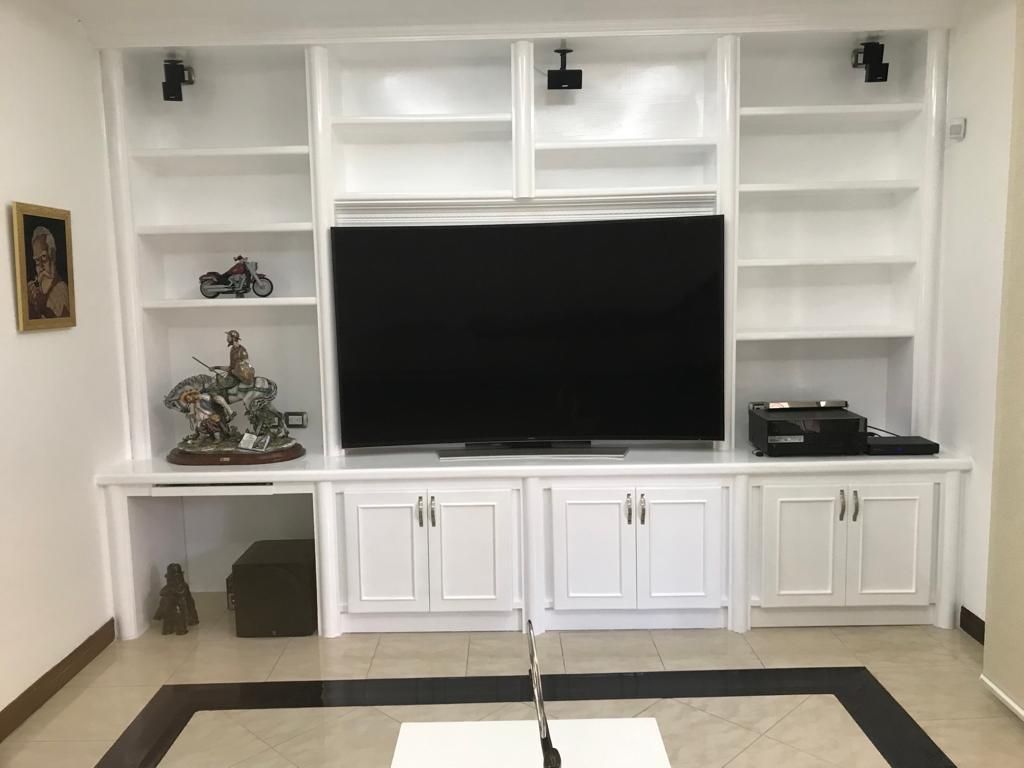 Pared de entretenimiento empotrada en blanco con televisor, estantes, armarios y objetos decorativos en una sala de estar.
