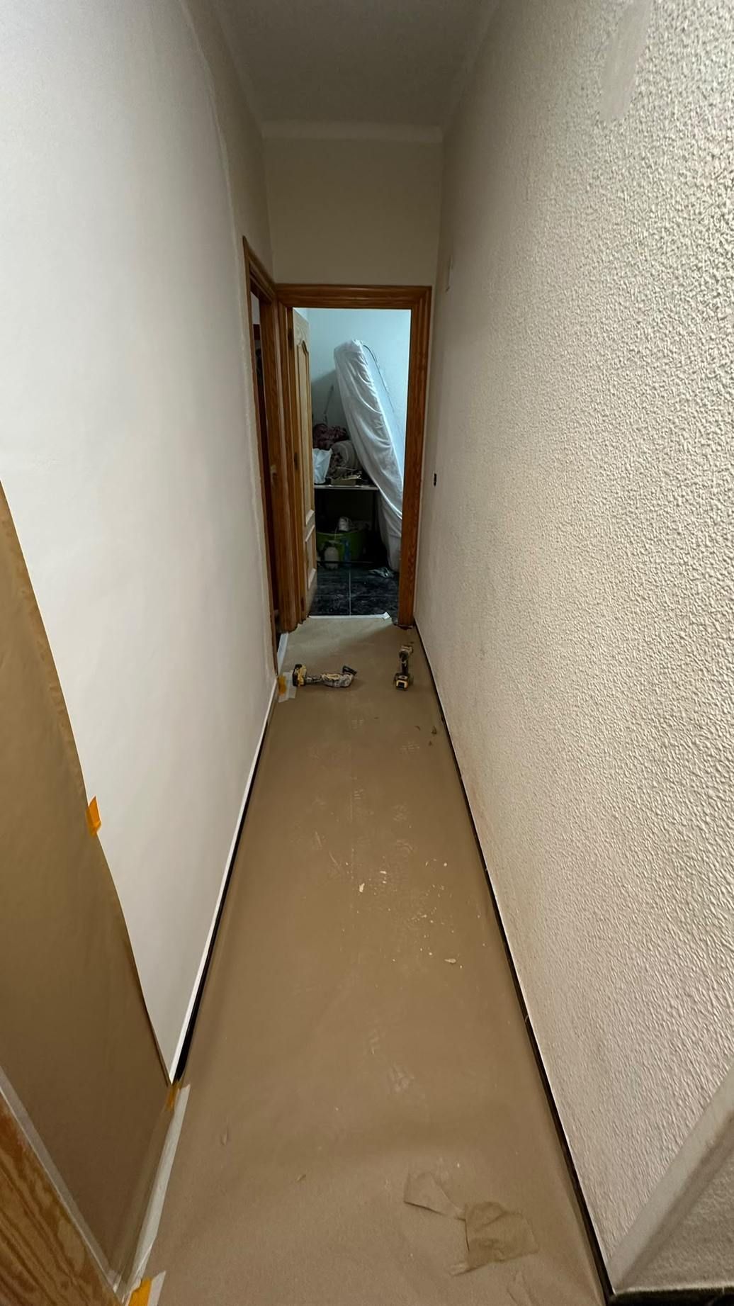 Pasillo estrecho con alfombra beige y paredes blancas que conduce a una puerta abierta y a escombros al fondo.