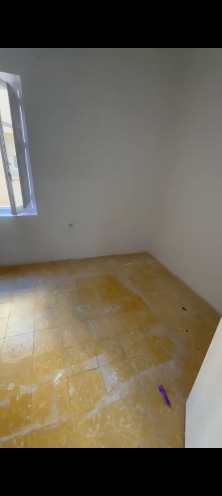 Habitación vacía con paredes blancas, una ventana y suelo de baldosas amarillas