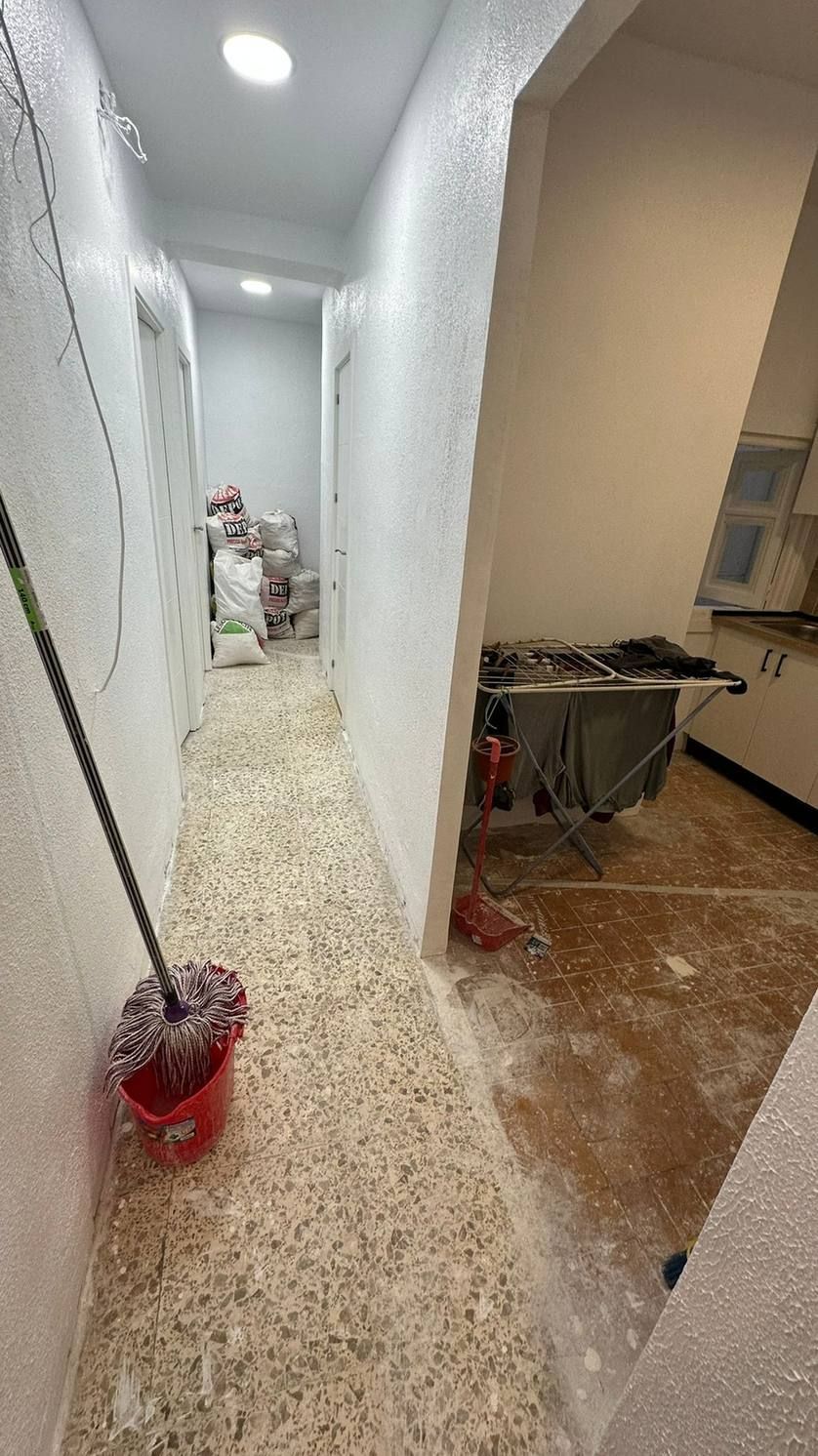 Pasillo estrecho en obras, con cubos de pintura y herramientas en el suelo y una zona de trabajo a la derecha.
