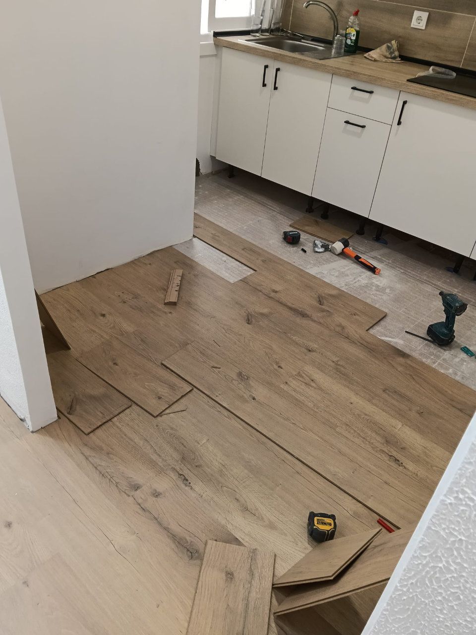 Suelo de madera parcialmente instalado en una cocina, con herramientas y materiales esparcidos por el suelo.