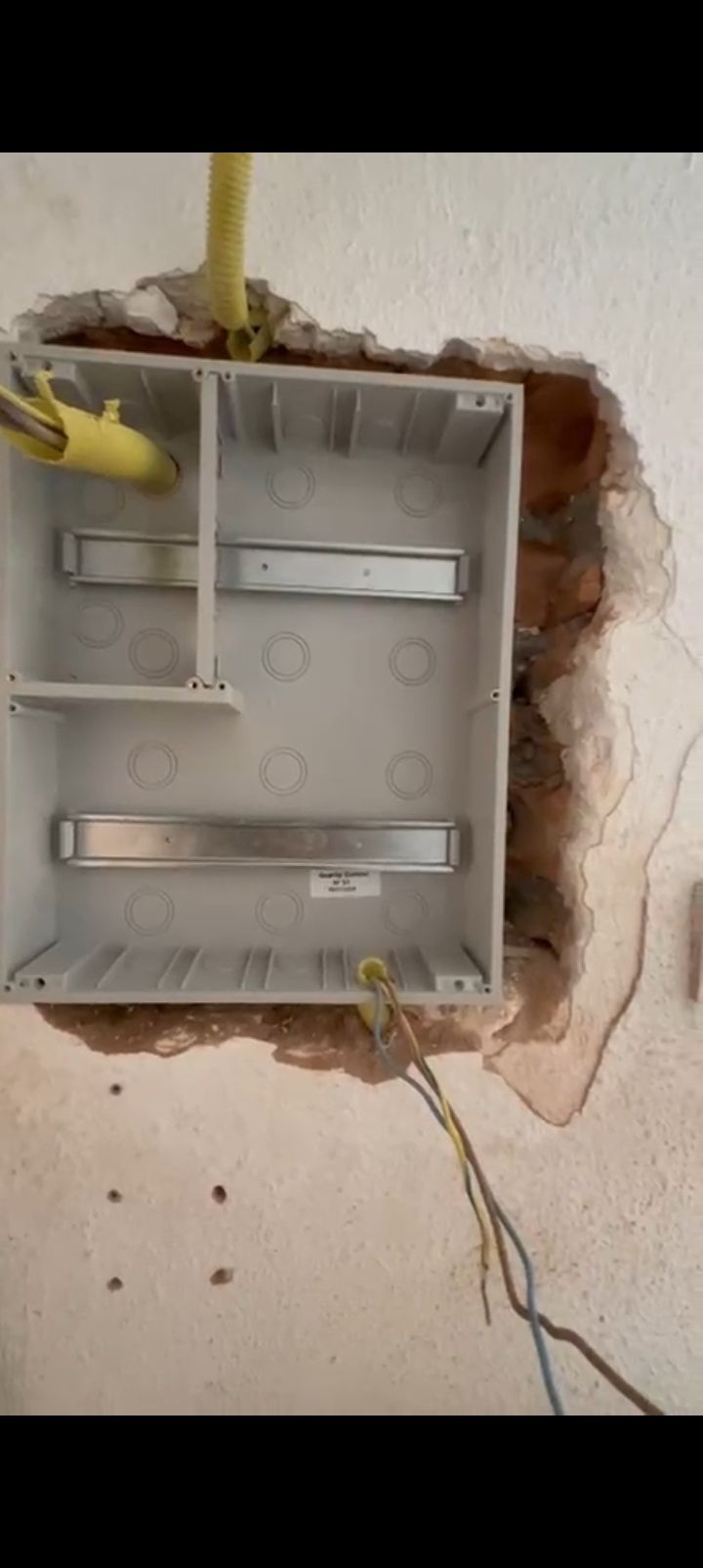 Caja eléctrica de pared abierta con cables expuestos y yeso desconchado alrededor de la abertura