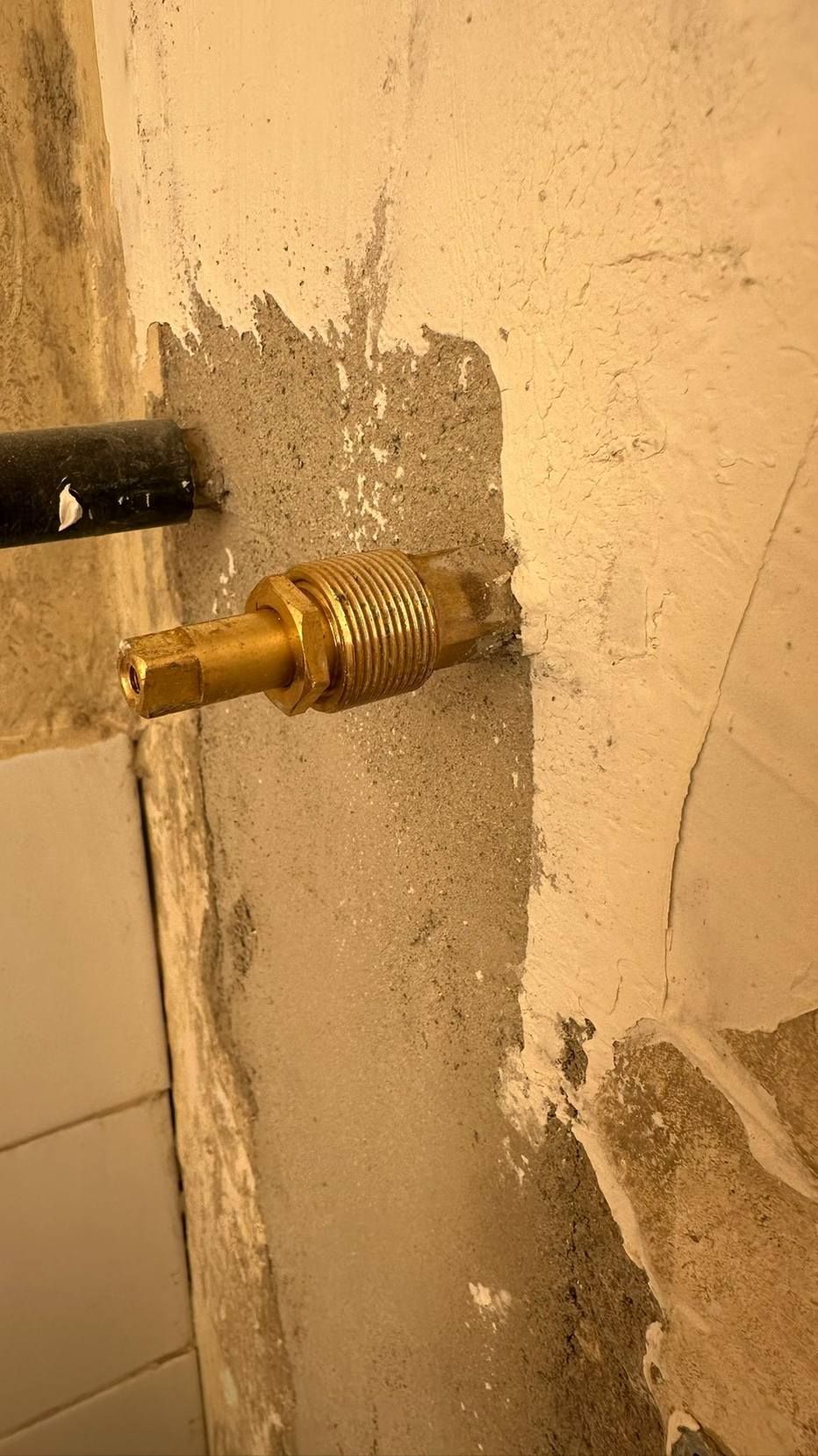 Racor de latón que sobresale de una pared de yeso rugosa con un parche de reparación a la vista