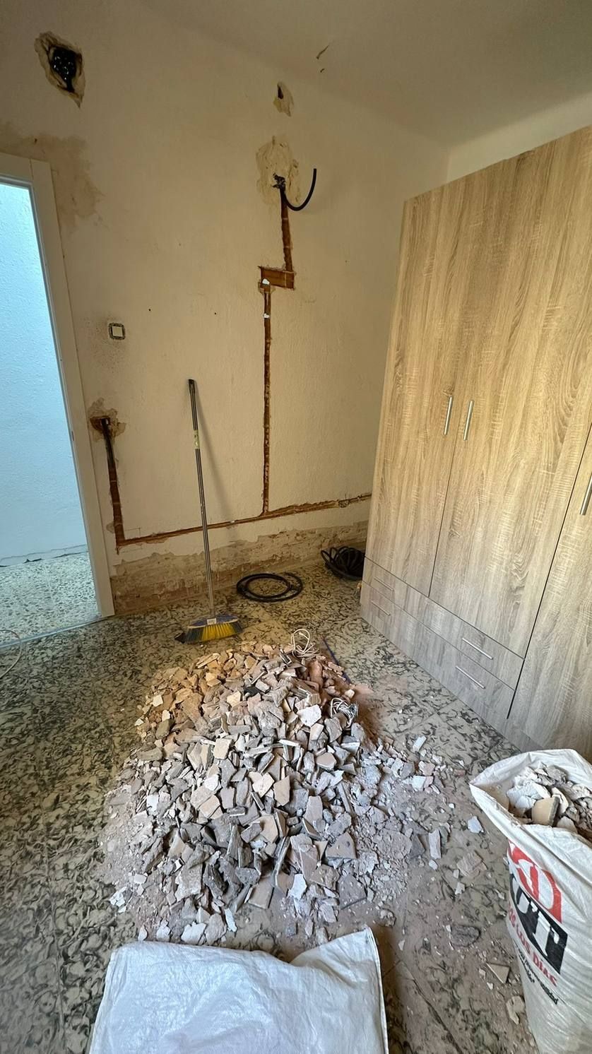 Habitación interior en obras, con cables a la vista, escombros en el suelo y un cubo blanco en una esquina
