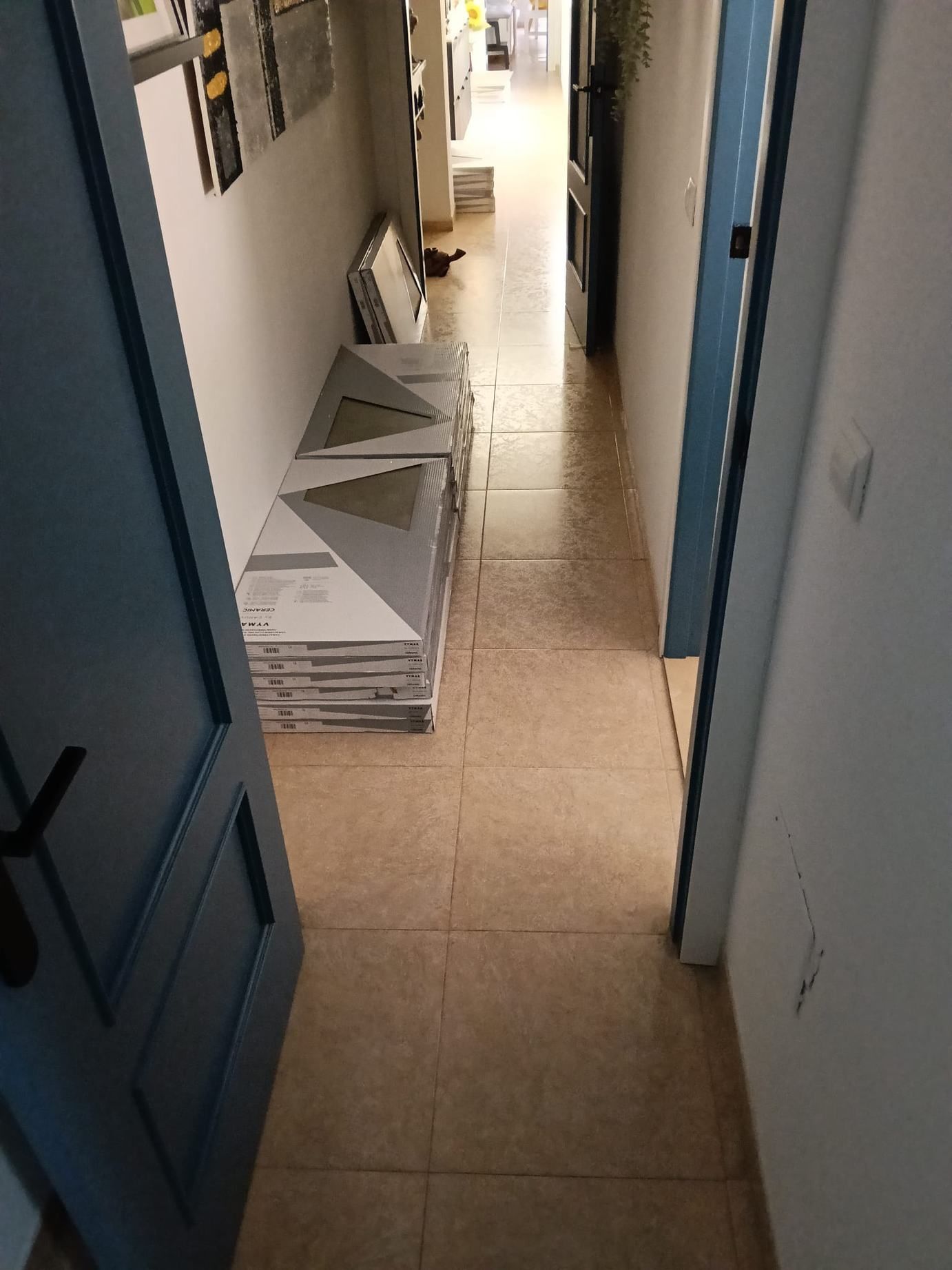 Pasillo estrecho con suelo de baldosas y paneles blancos apilados apoyados contra la pared.