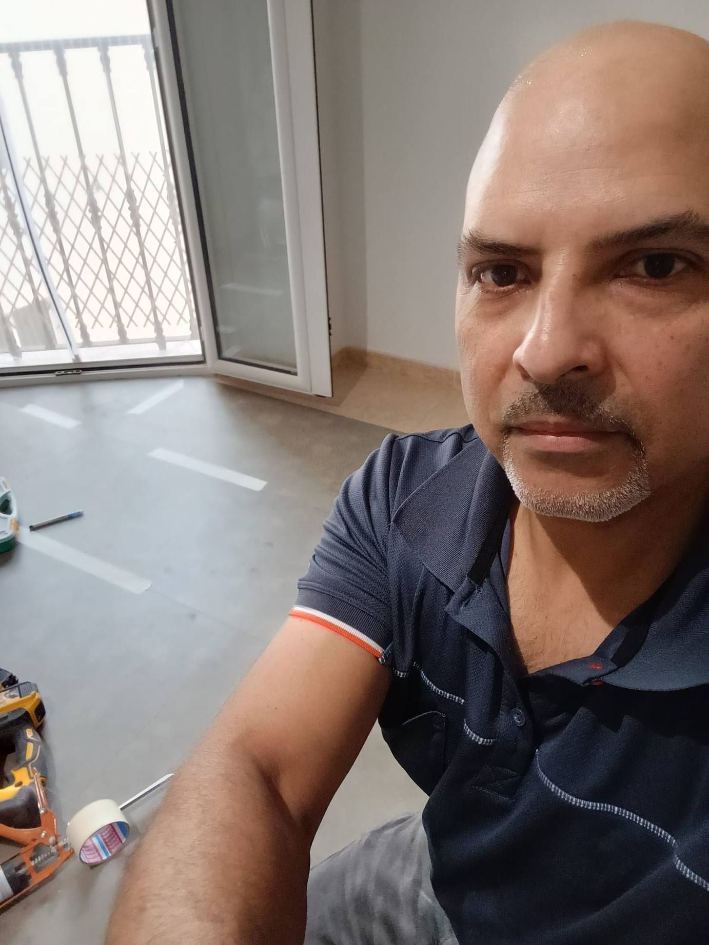 Hombre haciéndose un selfi en una habitación luminosa con una ventana abierta y el suelo de madera sin cubrir