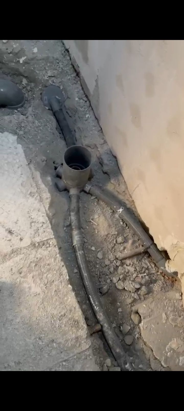 Tubo de desagüe abierto en una esquina de hormigón agrietada, junto a una pared