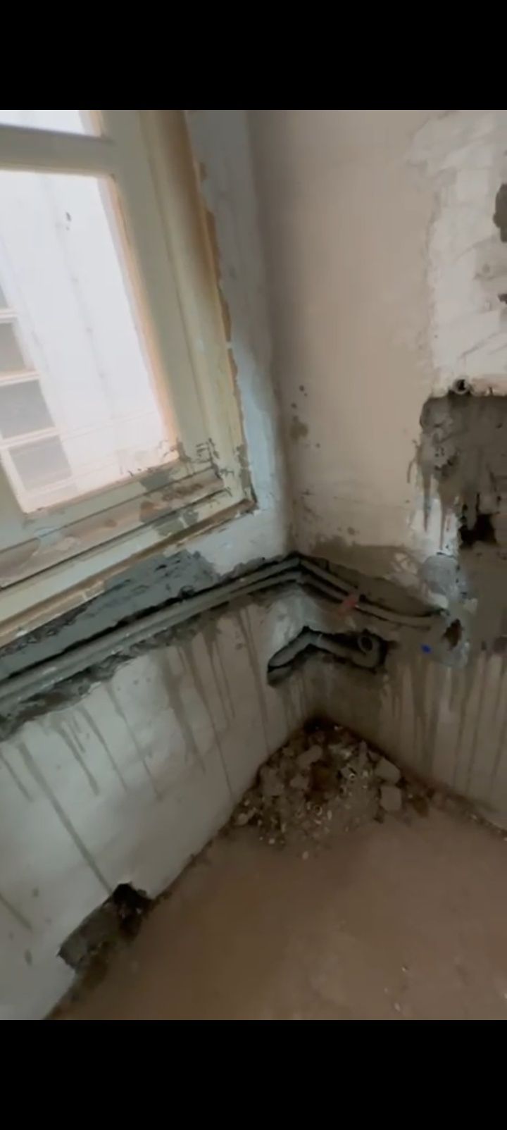 Esquina de una pared dañada, con pintura descascarada y moho debajo de una ventana, con señales de daños por agua.