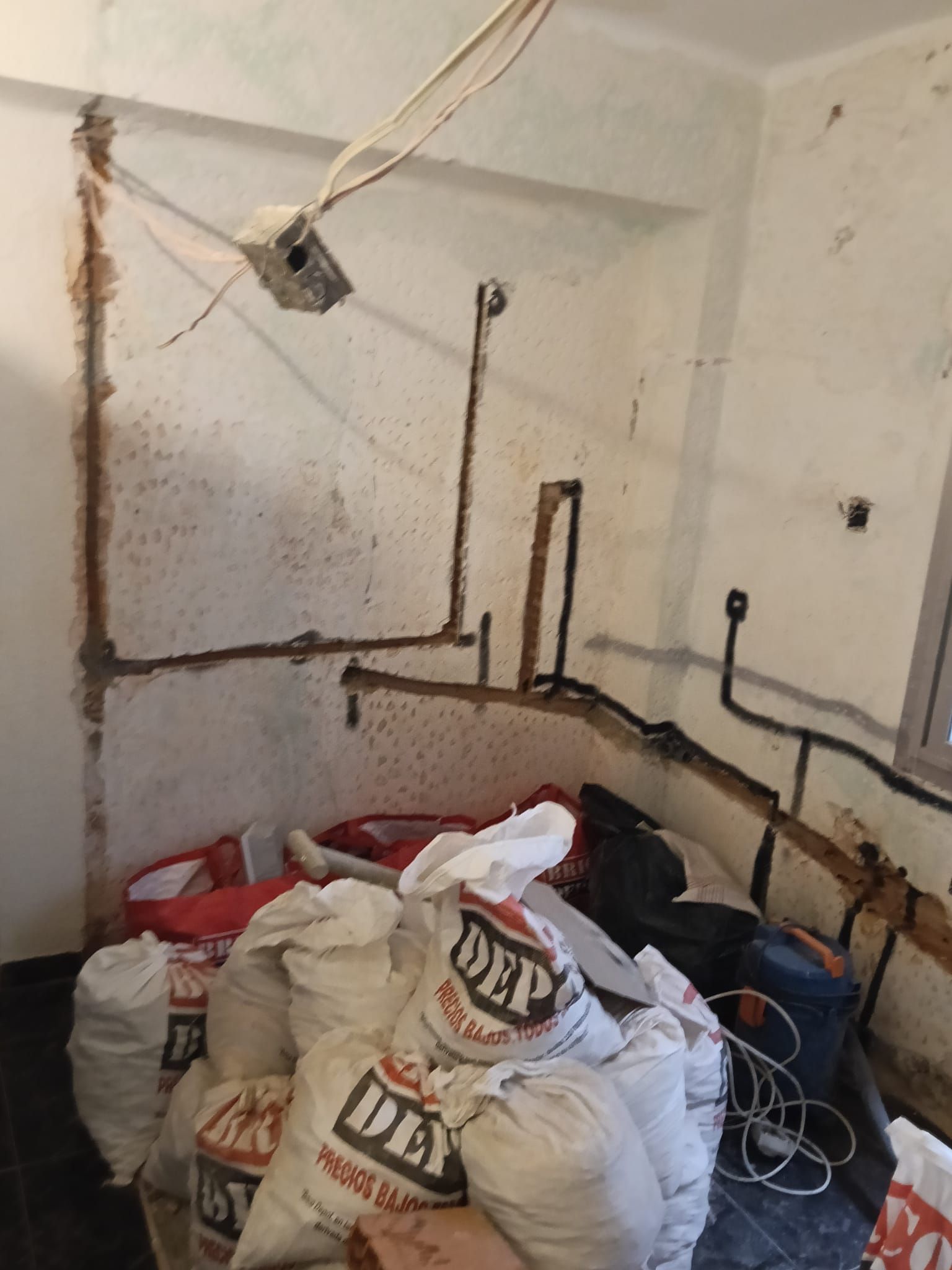 Habitación desordenada con bolsas grandes, tuberías a la vista y paredes sucias, que parece estar en obras o usarse como trastero