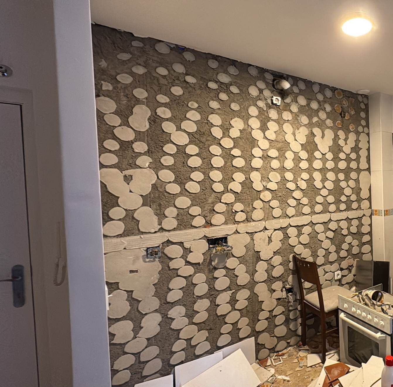 Pared de cocina parcialmente alicatada con un patrón de piedra gris, tuberías del fregadero y una encimera con una estufa a la derecha