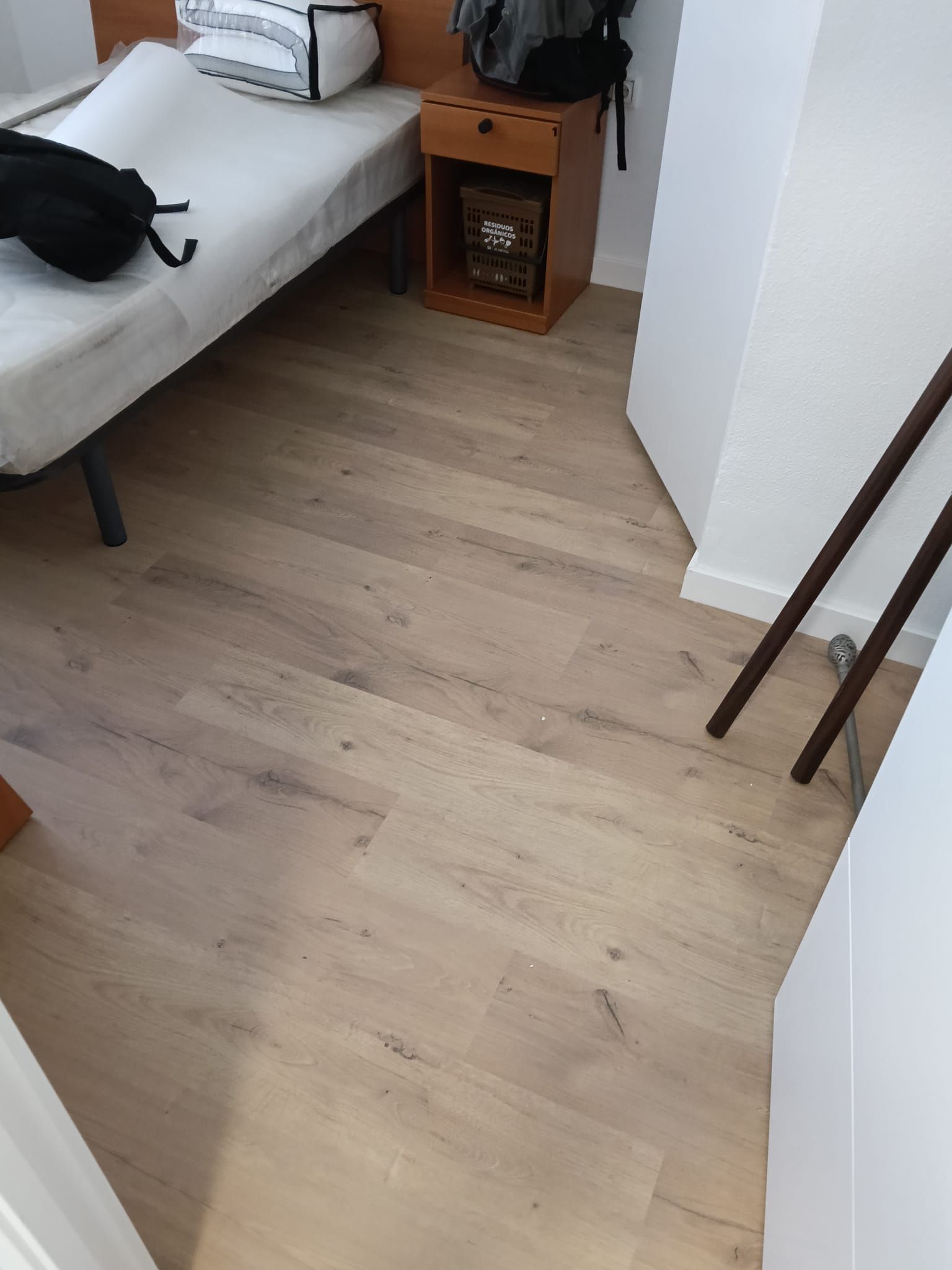 Dormitorio pequeño con suelo de madera clara, cama, mesita de noche y paredes blancas.