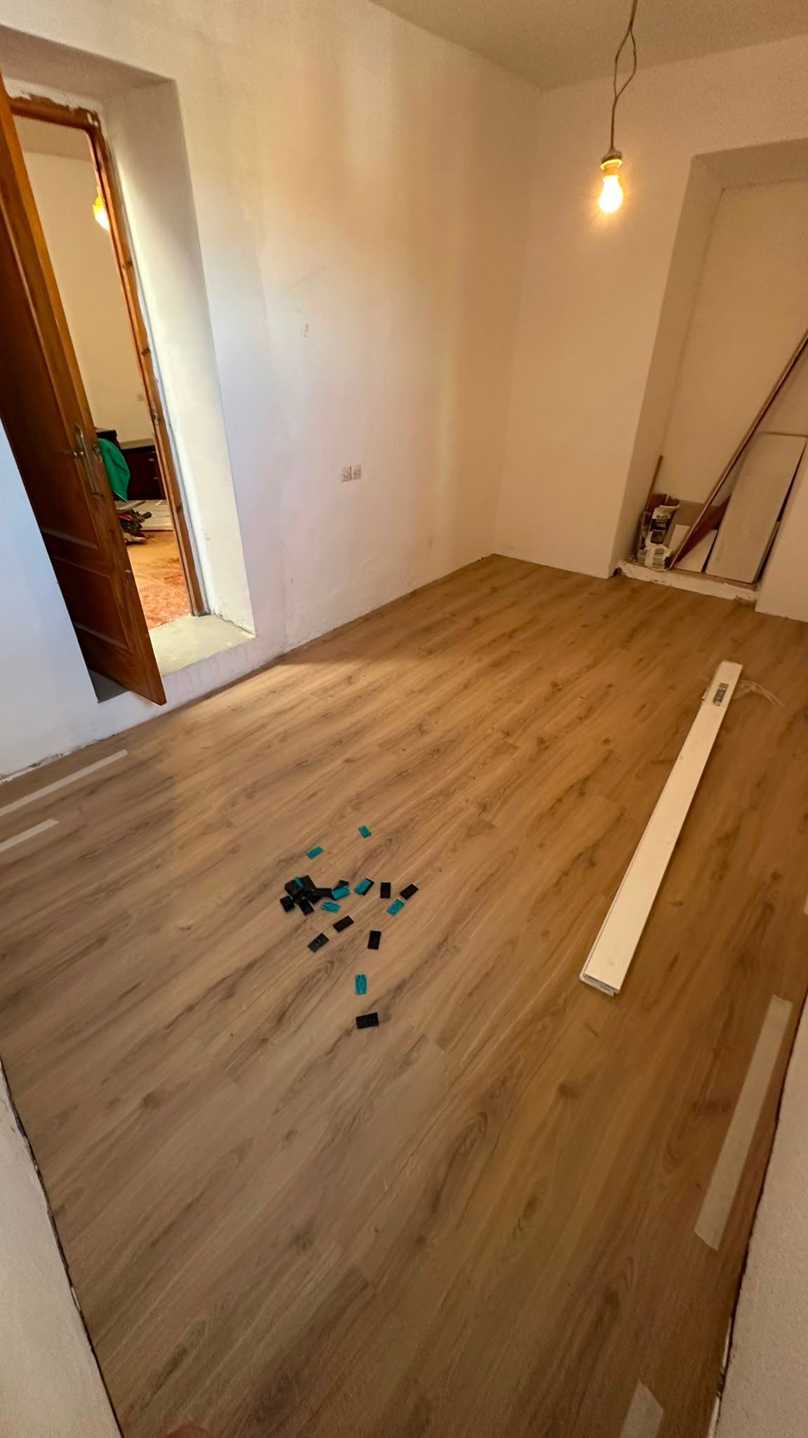 Habitación vacía con suelo de madera, una puerta abierta y un tablón blanco largo en el suelo.