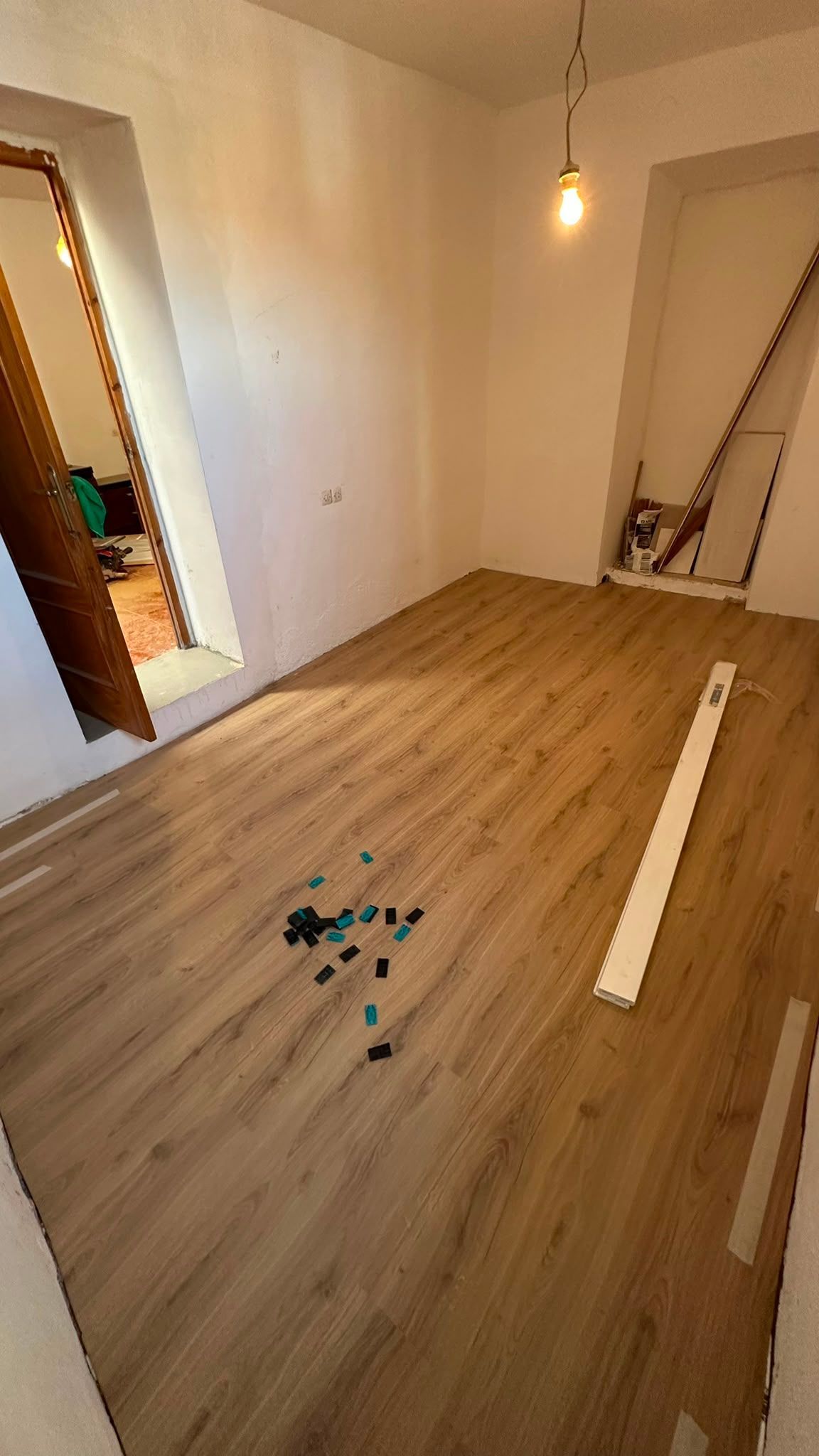 Habitación vacía con suelo de madera, paredes blancas y materiales de construcción esparcidos por el suelo.