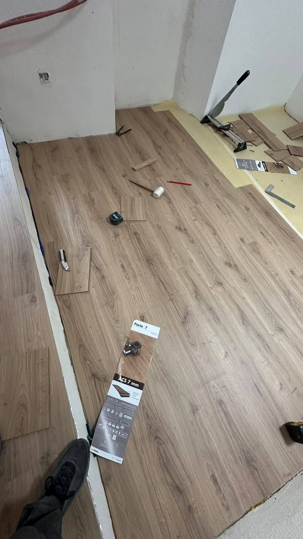 Habitación pequeña con suelo de madera y herramientas, cables y embalajes esparcidos durante la instalación del suelo.