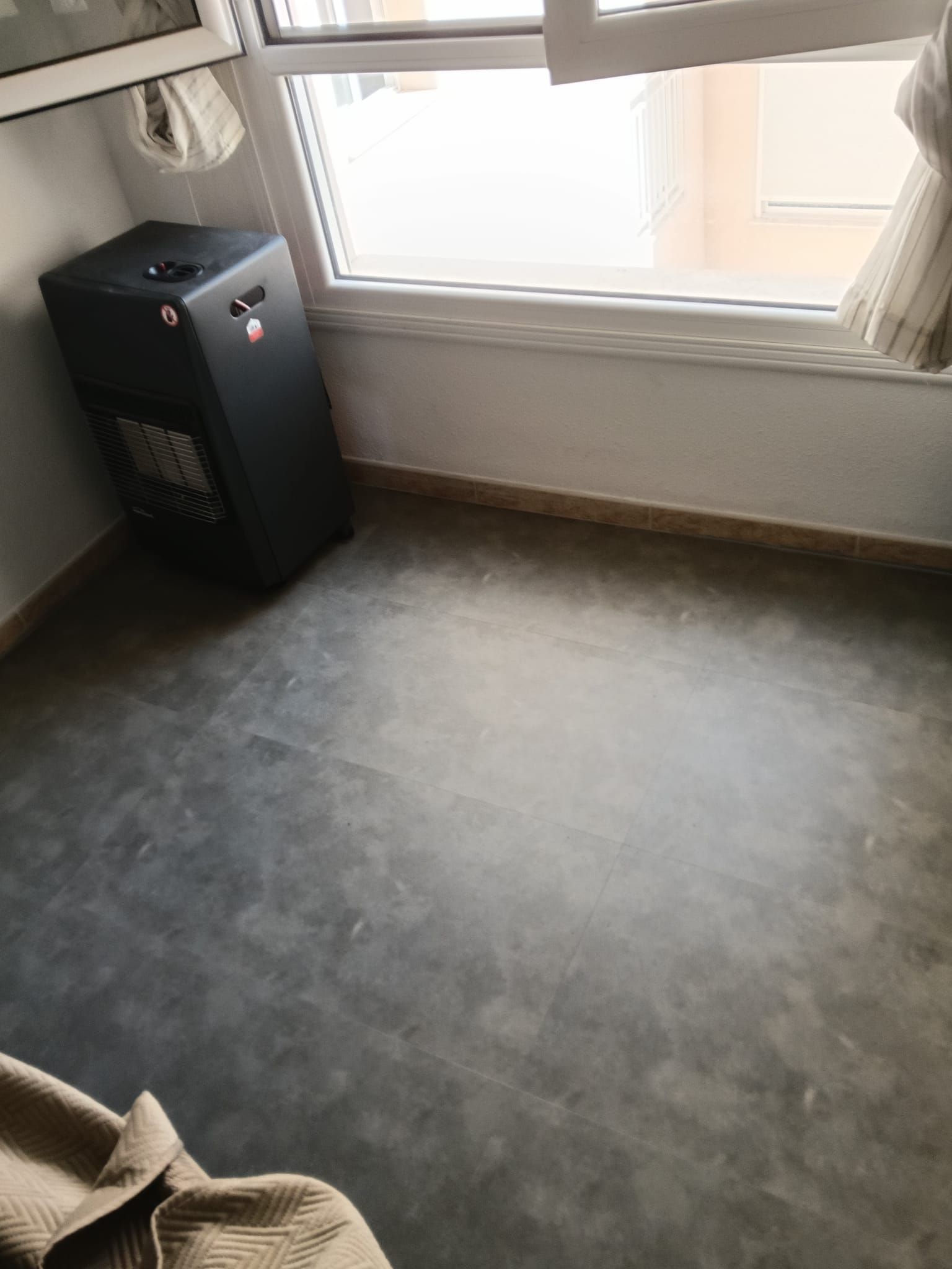 Habitación vacía con moqueta, una ventana y un pequeño aparato negro junto a la pared