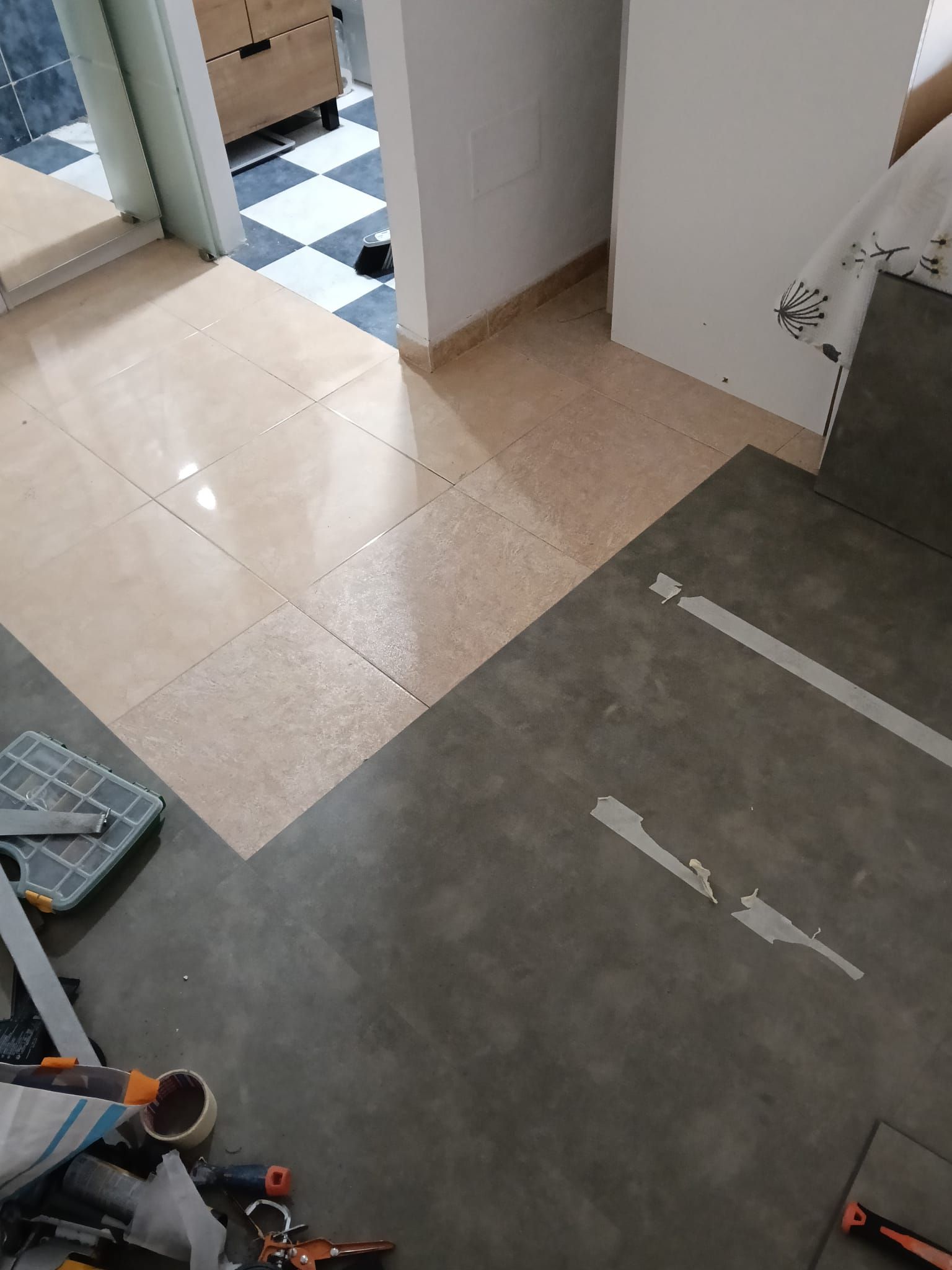 Pasillo interior con suelo de baldosas beige que da paso a un suelo gris y una puerta a la izquierda.