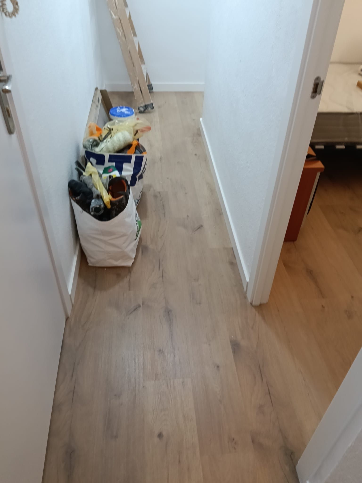 Pasillo estrecho con una bolsa blanca llena de diversos artículos en el suelo, junto a la pared.
