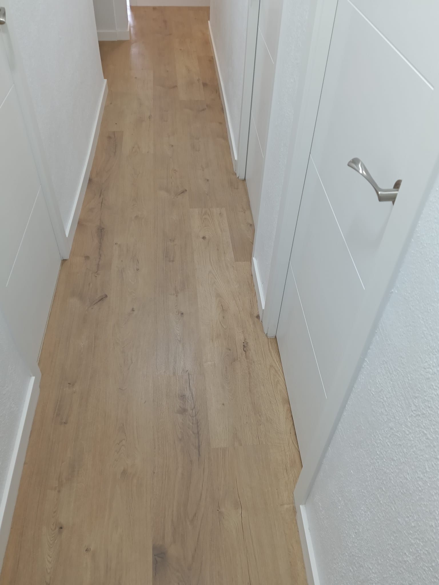 Pasillo estrecho con suelo de madera clara y puertas blancas a ambos lados.